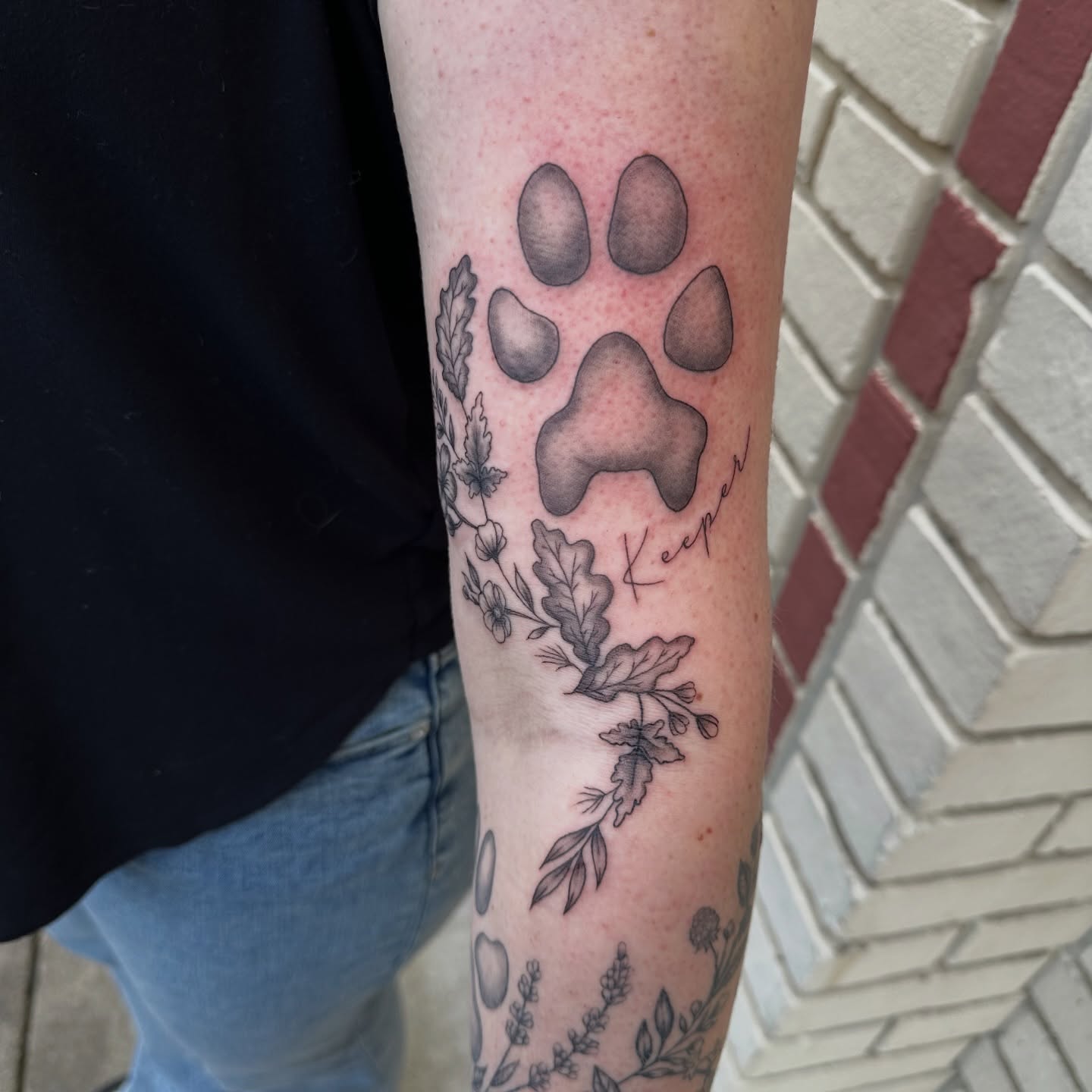 Paw print with foliage black and grey tattoo on the forearm by Lauren DeLizza