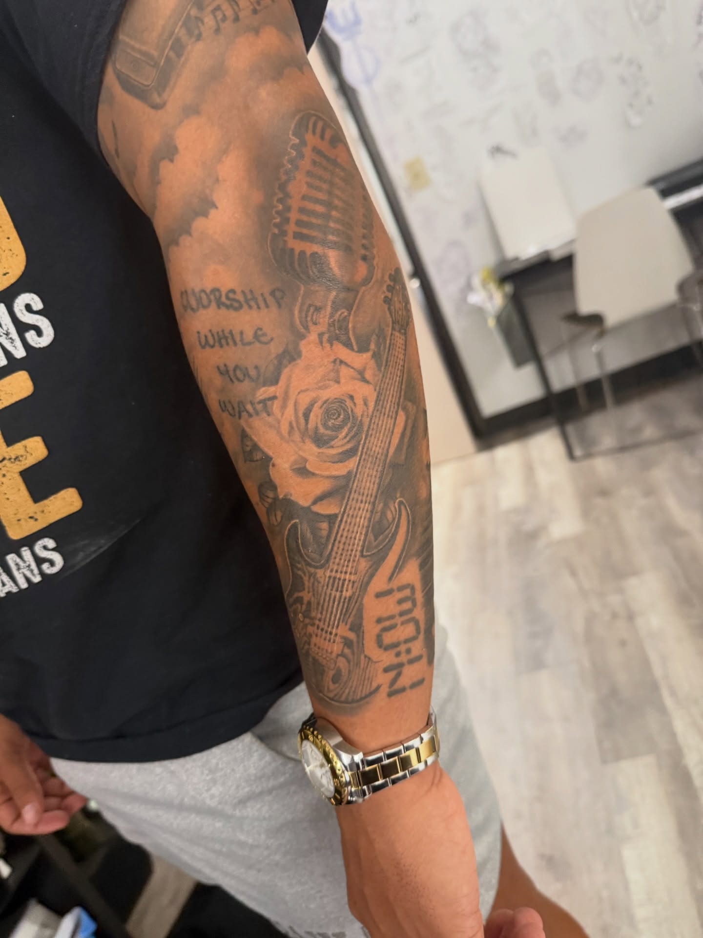 Microphone, guitar, rose, text black and grey tattoo on the forearm by Atlanta Tattoo Artist