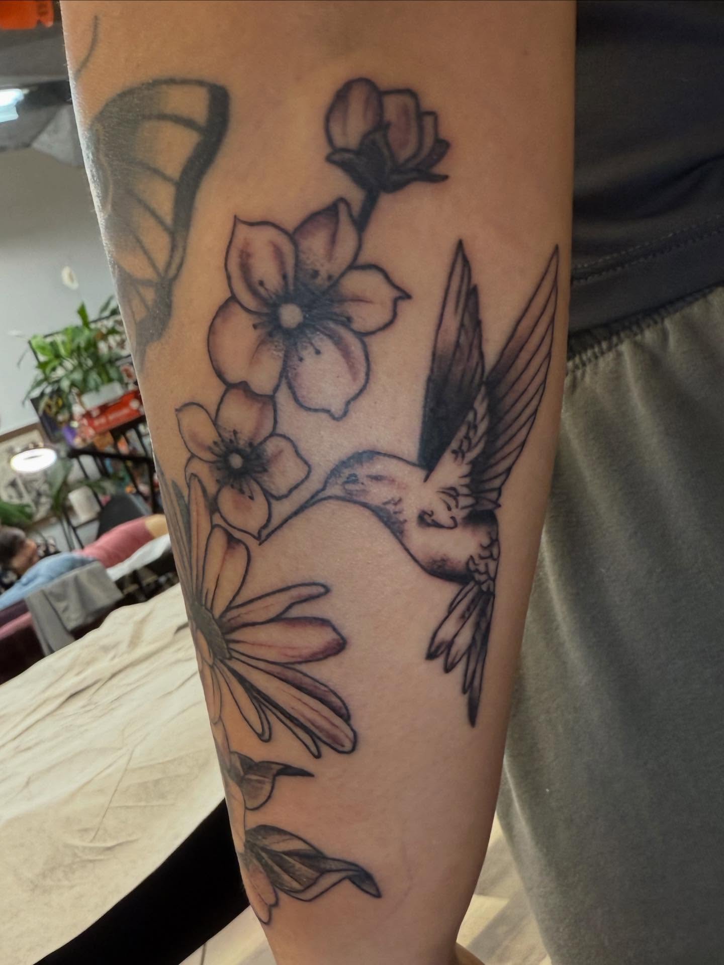 Hummingbird and flowers black and grey tattoo on the forearm by Rigo Vargas