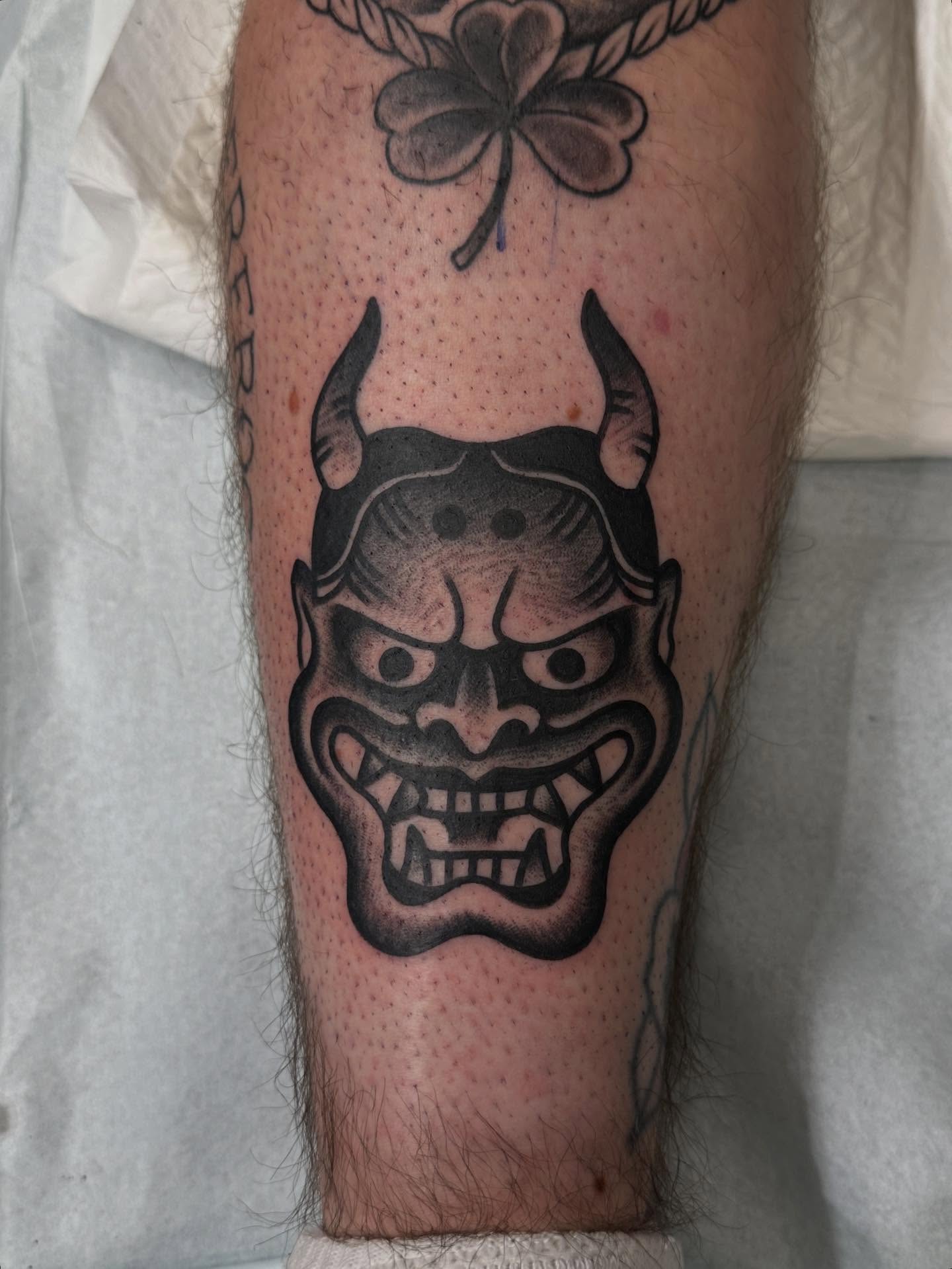 Demon mask black and grey tattoo on the calf by Matt Kearney
