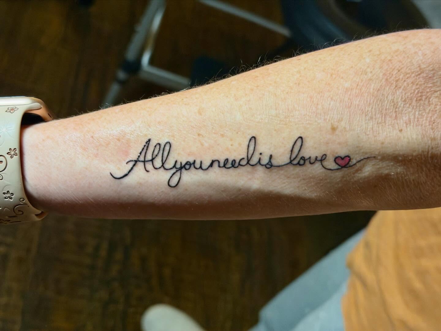 All you need is love lettering script tattoo on the forearm by C.J.K. Roy