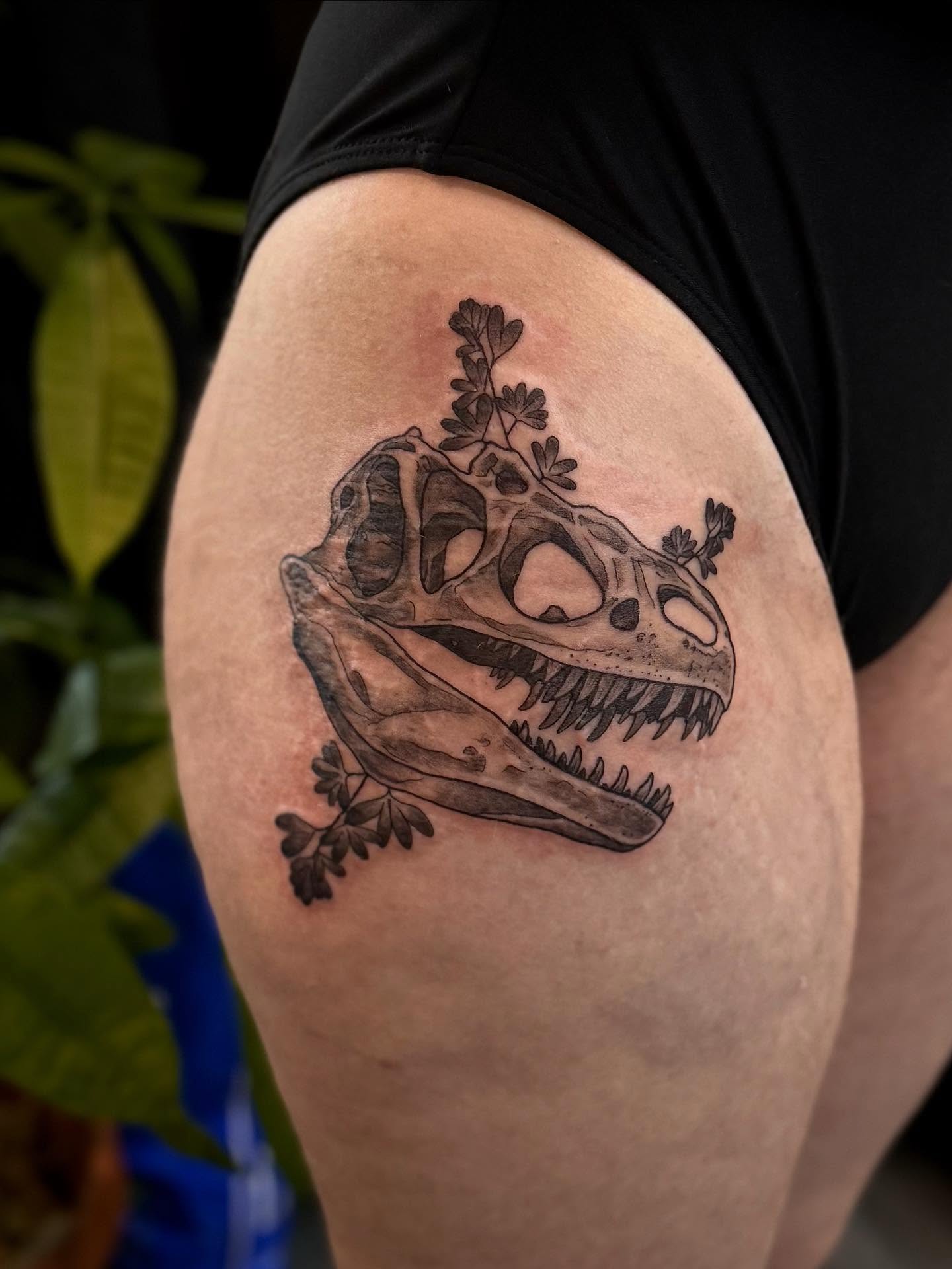 Dinosaur skull black and grey tattoo on the thigh by Ashley Kayser