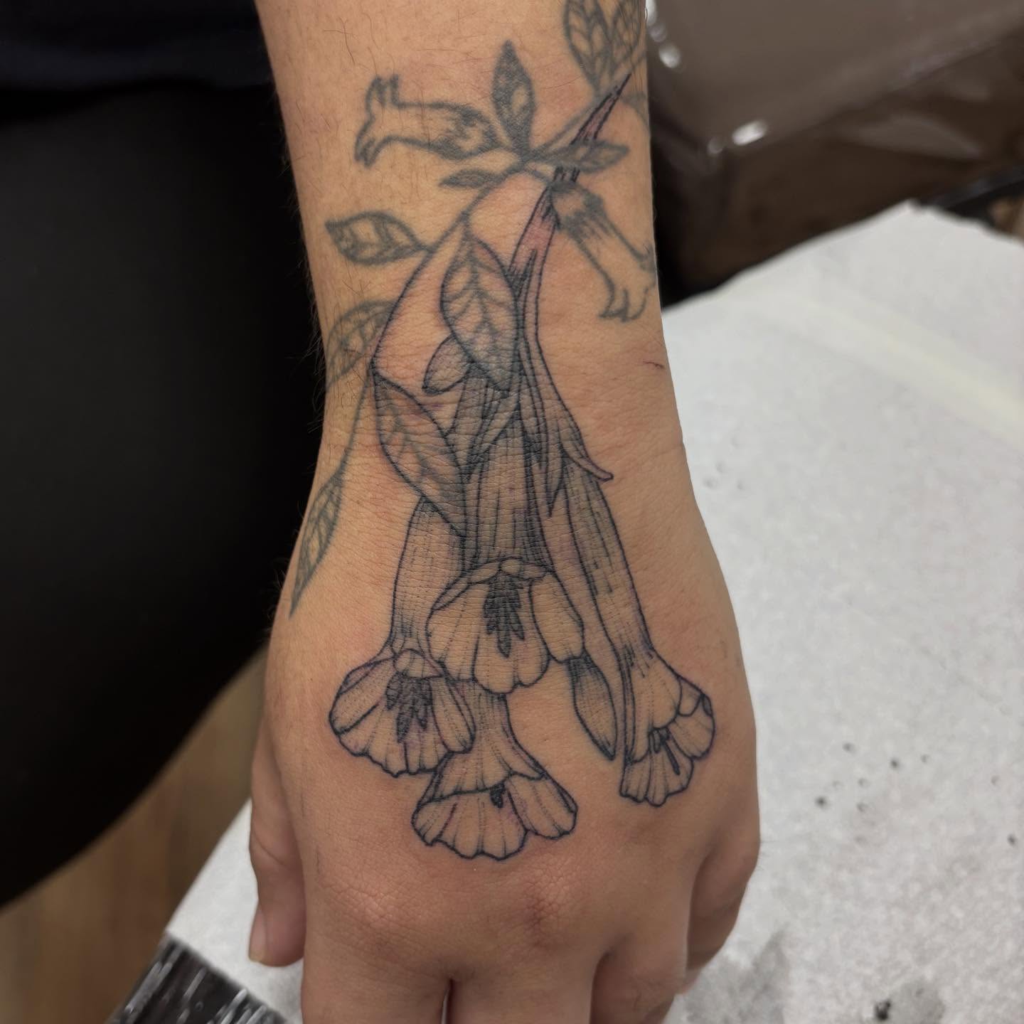 Bell-shaped flowers black and grey tattoo on the hand by Dallas Davis