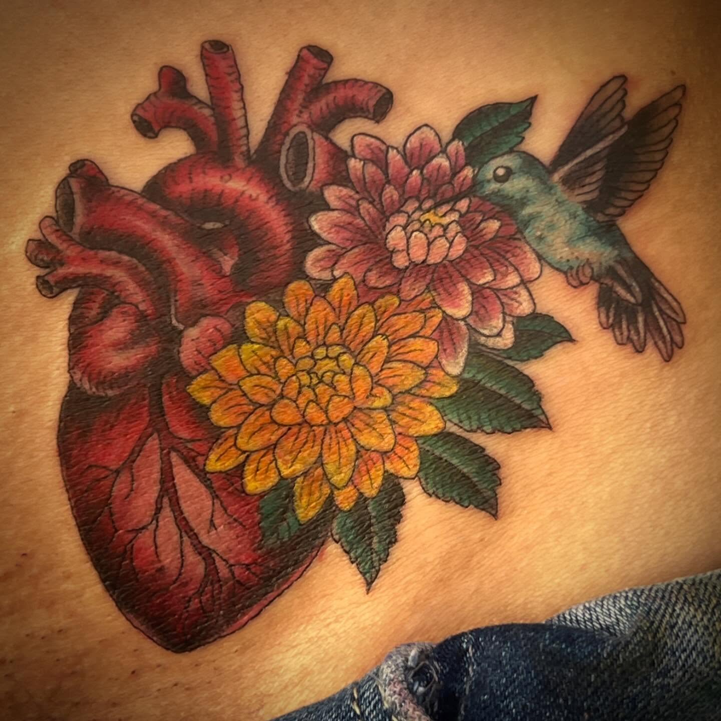 Heart with flowers and hummingbird American traditional tattoo on the torso by Kayle Leogrande