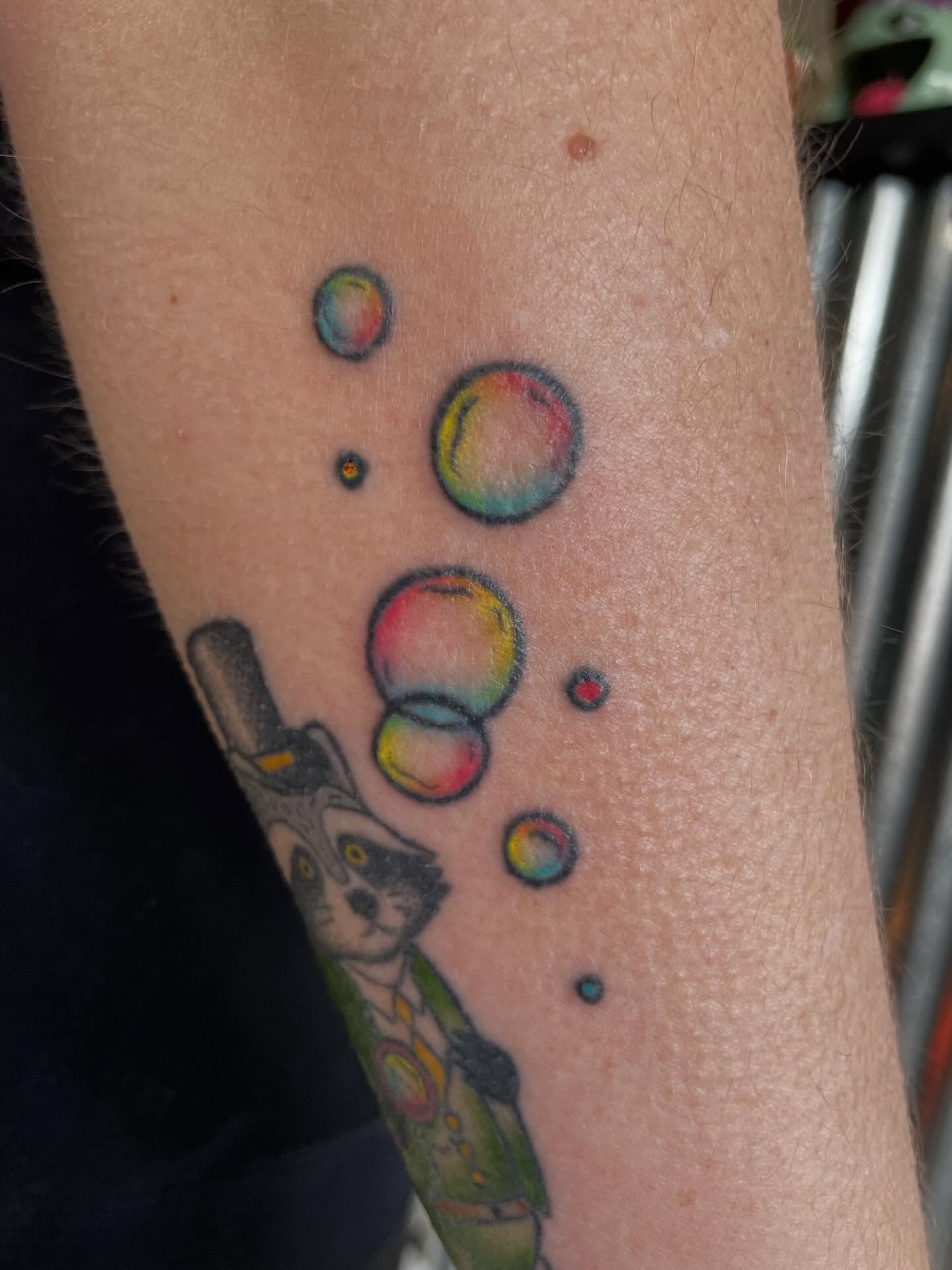Raccoon with bubbles new school tattoo on the forearm by Mallory Moore