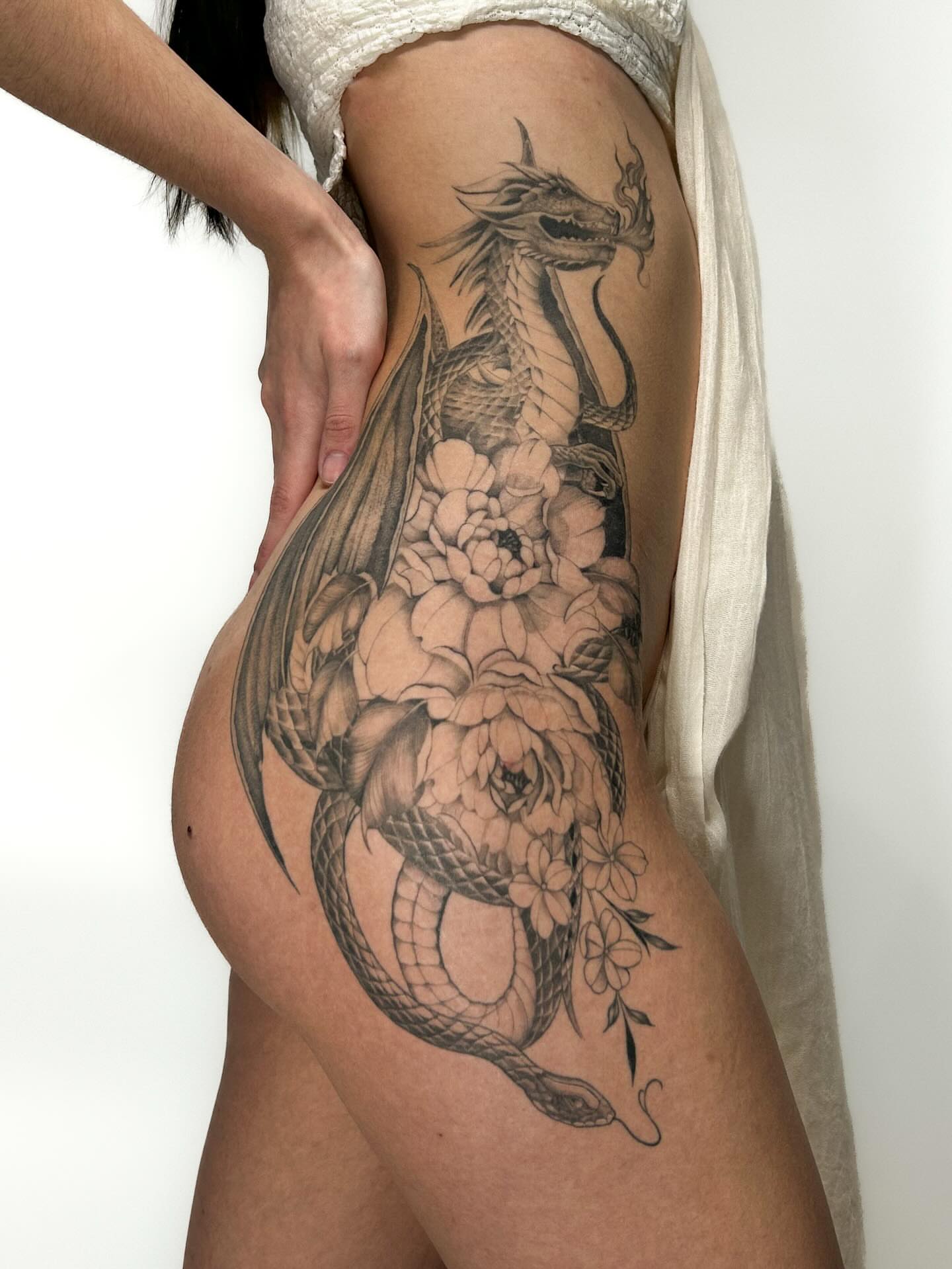 Dragon and flowers realism tattoo on the thigh by Chloe