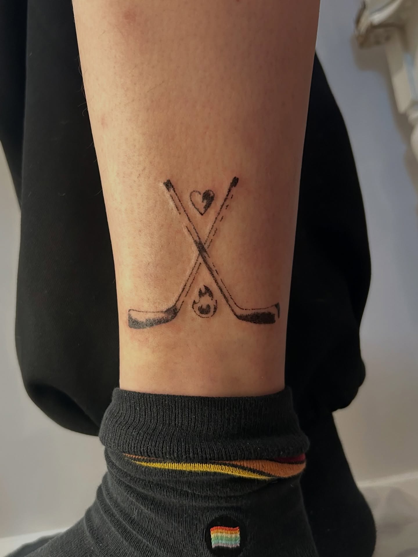 Hockey sticks and puck black and grey tattoo on the forearm by wanderfernfairy