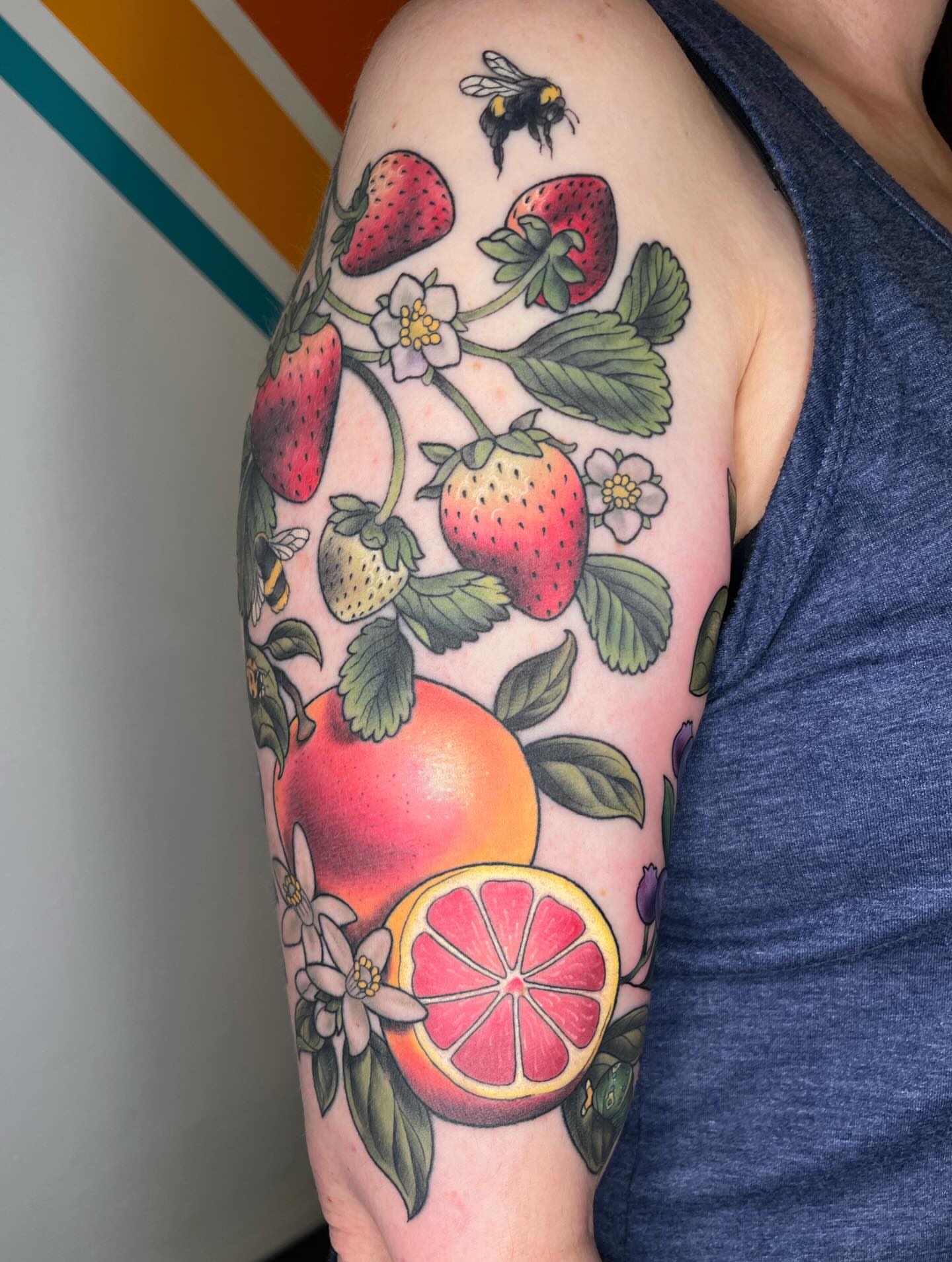 Fruit and strawberry plant realism tattoo on the upper arm by Emi Collison