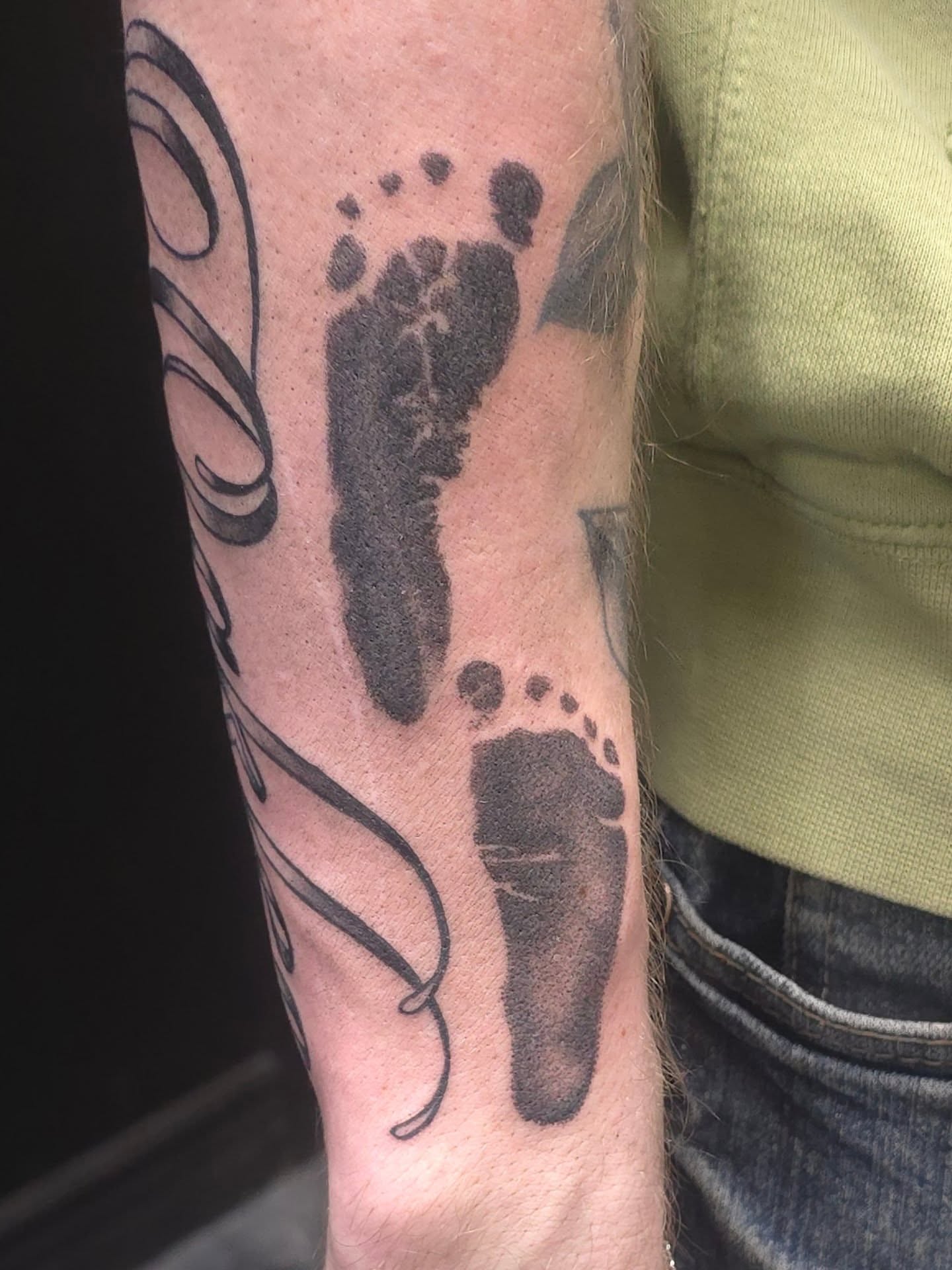 Footprints black and grey tattoo on the forearm by Trinity