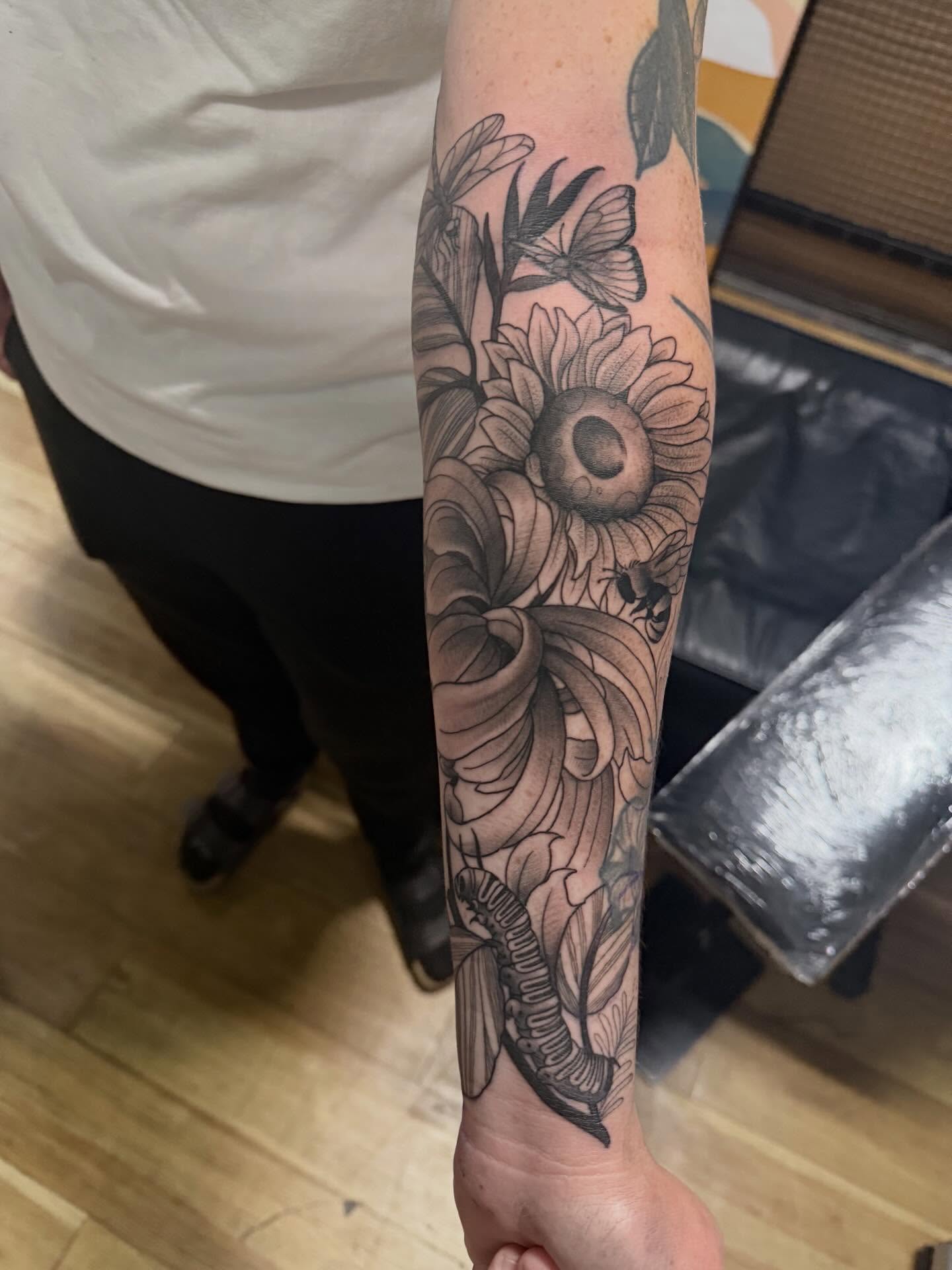 Sunflower and butterfly black and grey tattoo on the forearm by H.G