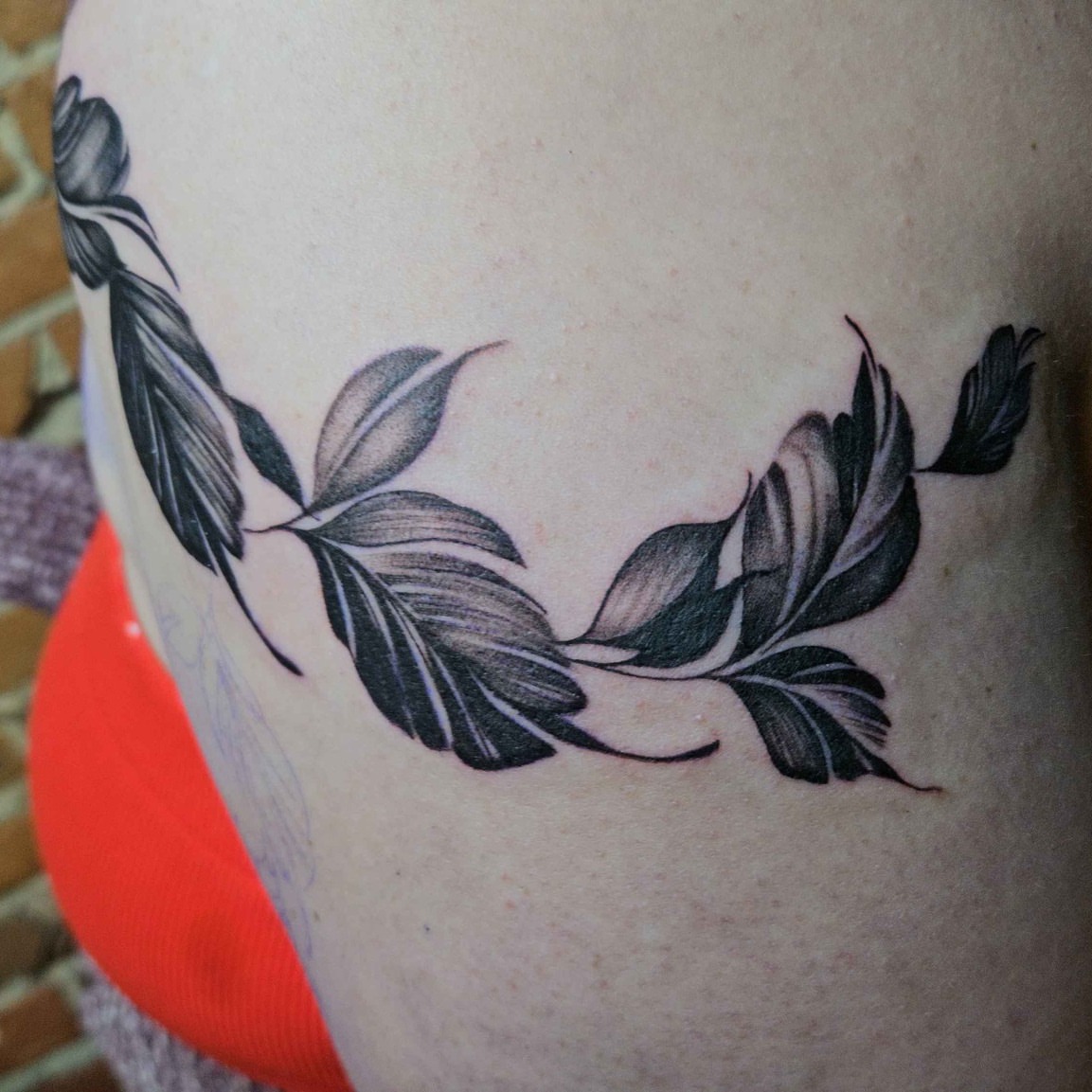 Feather wreath black and grey tattoo on the thigh by Iram Withencroft