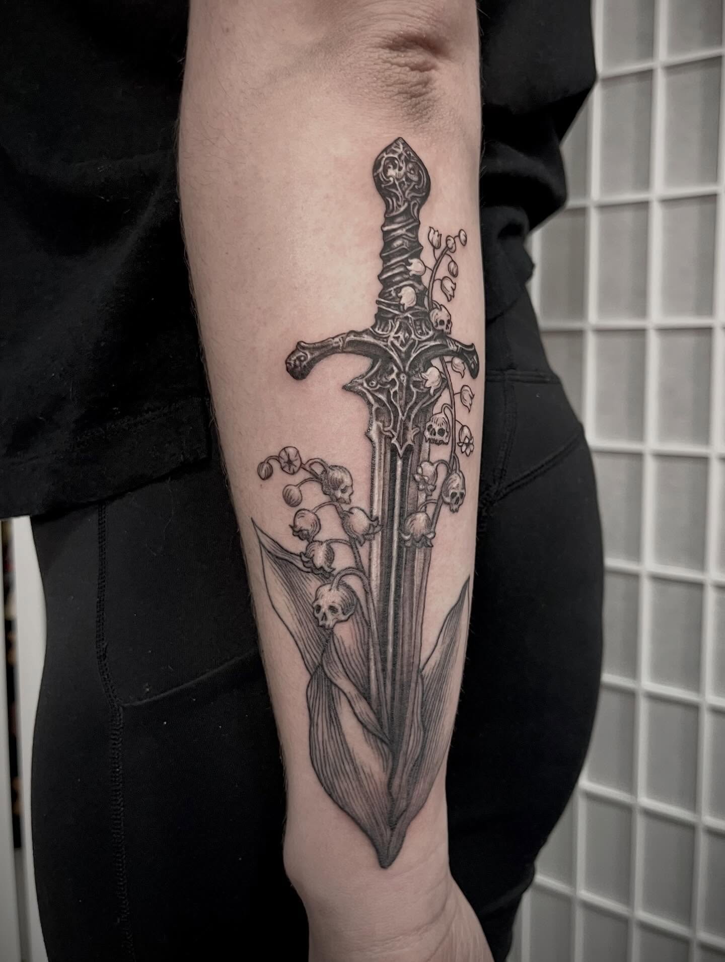 Lily of the valley and sword realism tattoo on the forearm by Tattoo Artist