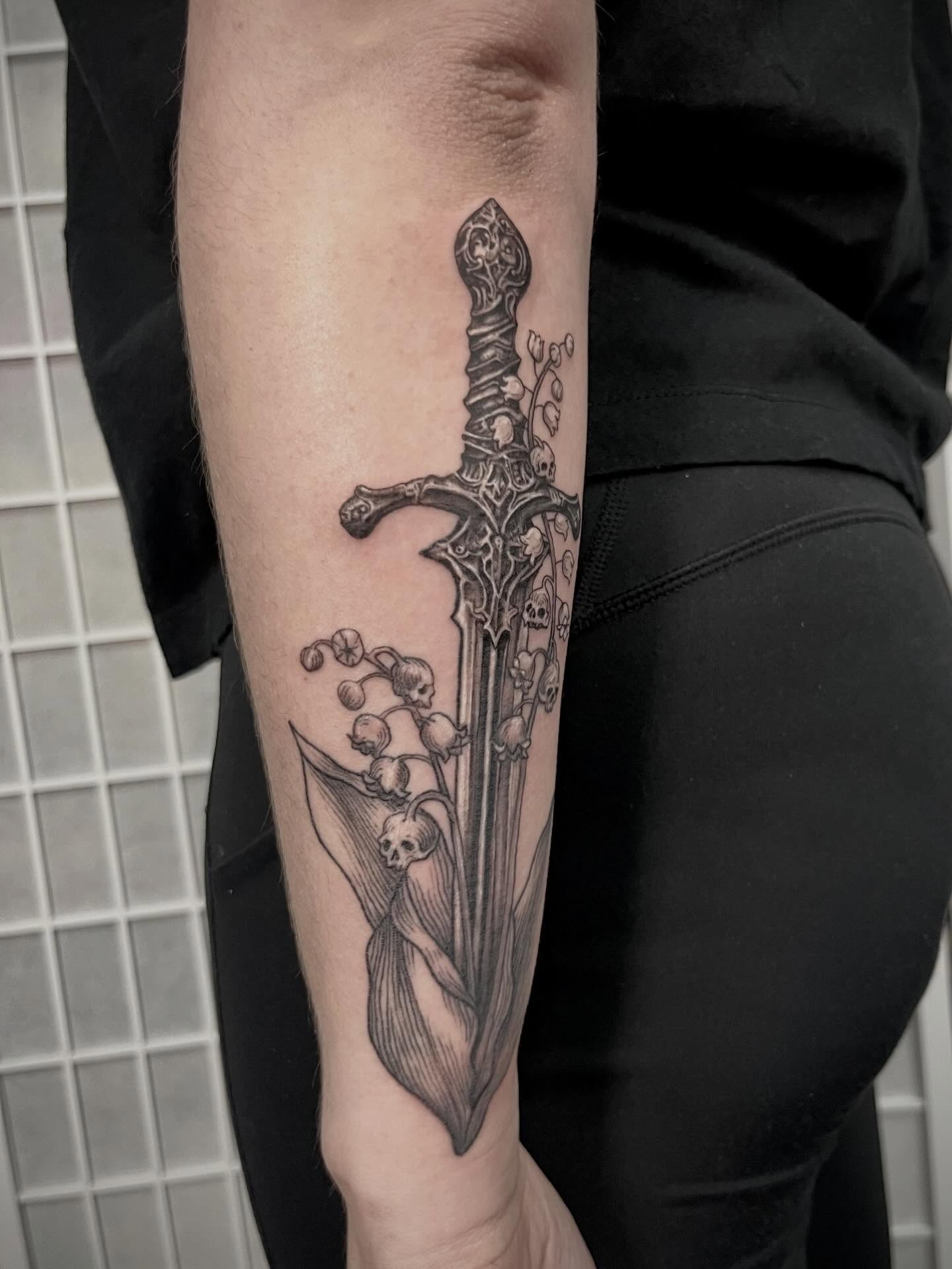 Sword and lilies of the valley realism tattoo on the forearm by Tattoo Artist