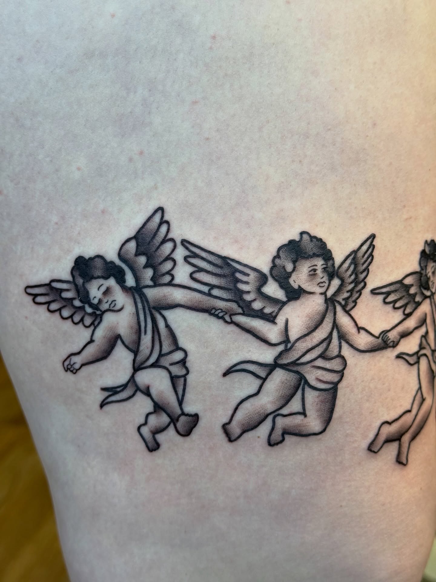Cherubs black and grey tattoo on the thigh by Kelsey Louis, Iowa City, Iowa