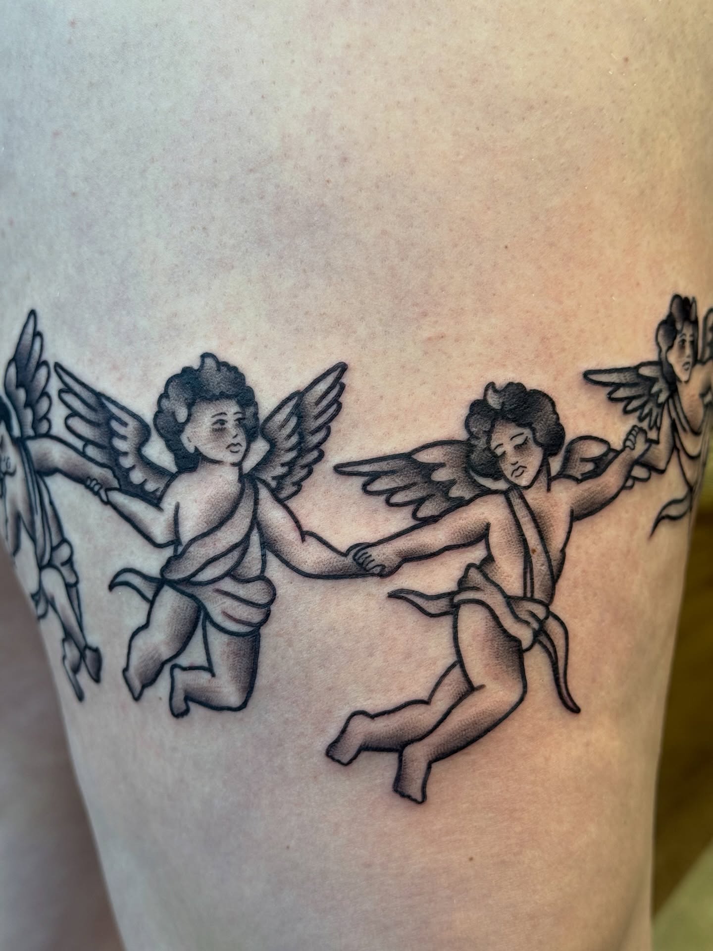 Cherubs black and grey tattoo on the thigh by Kelsey Louis, Iowa City, Iowa