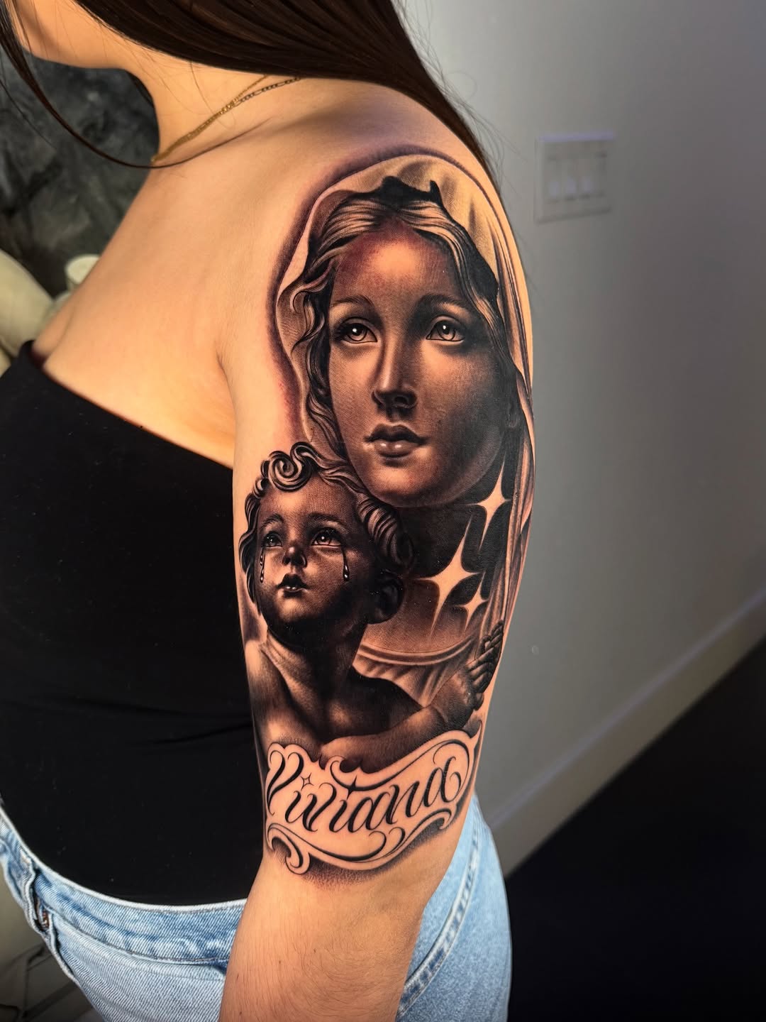 Virgin Mary and child with script Chicano tattoo on the shoulder by Fernando Andrade Jr