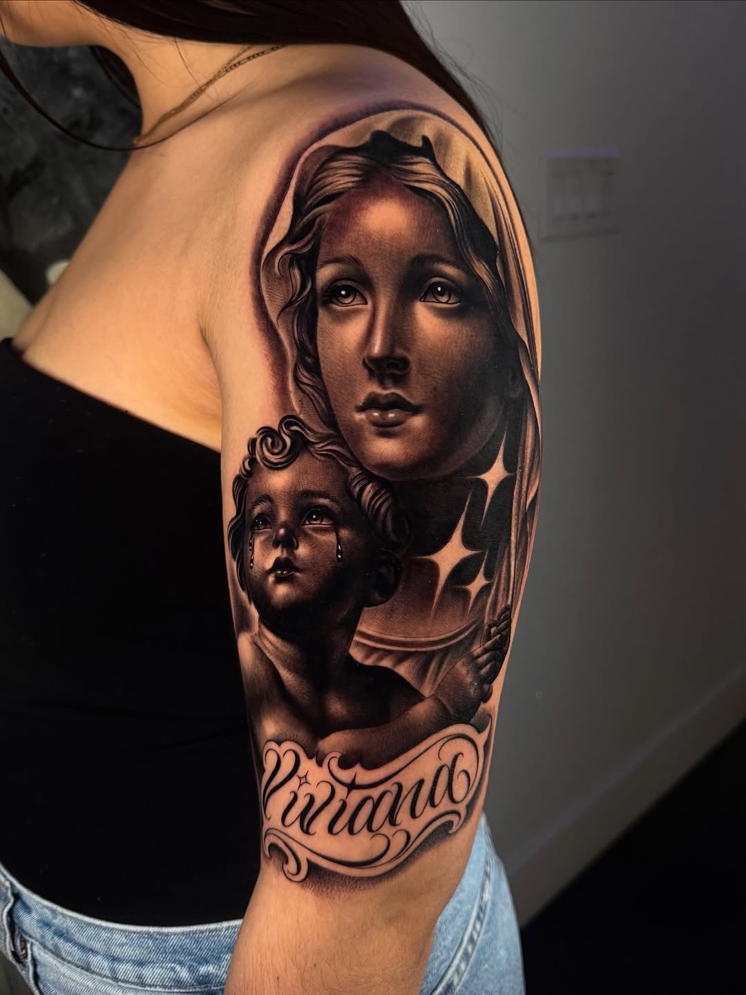 Virgin Mary and cherub with banner Chicano tattoo on the shoulder by Fernando Andrade Jr