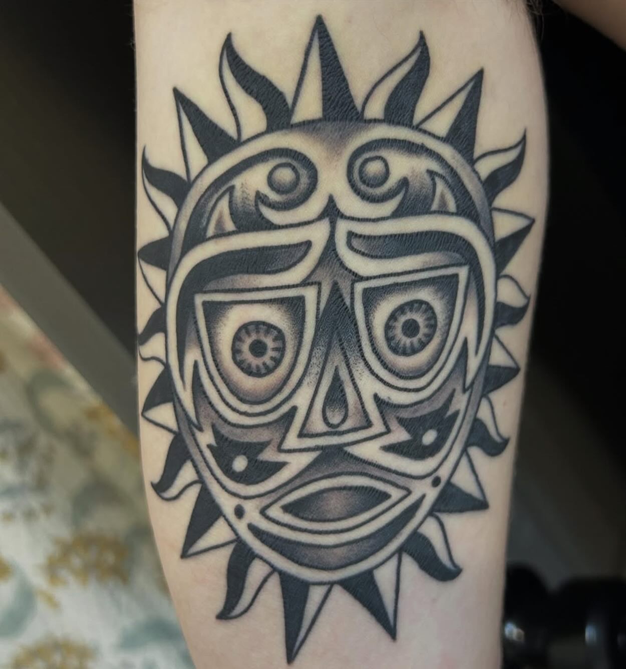 Sun mask black and grey tattoo on the forearm by Charlie Campanella