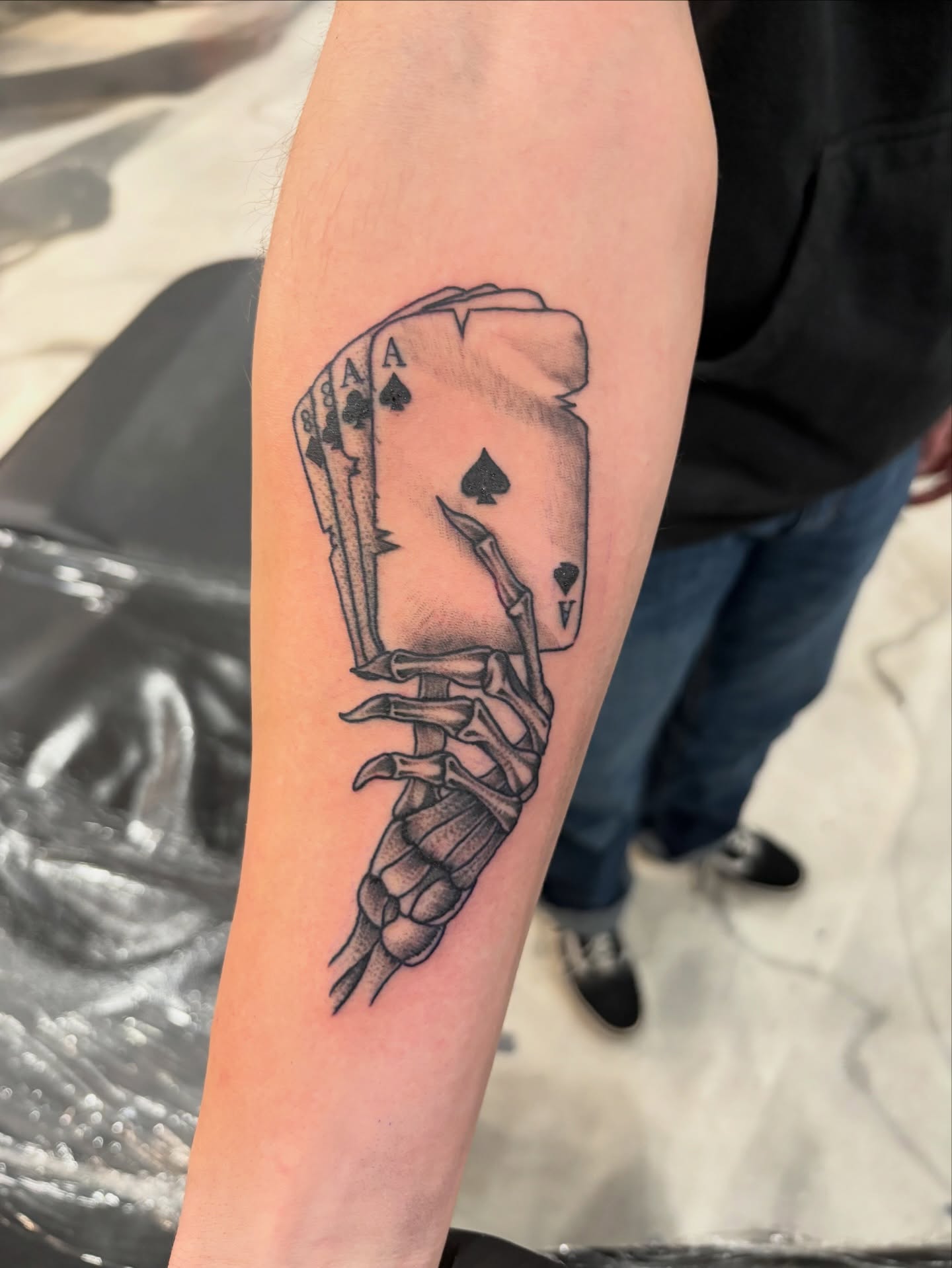 Playing card skeleton black and grey tattoo on the forearm by Miklo Montoya