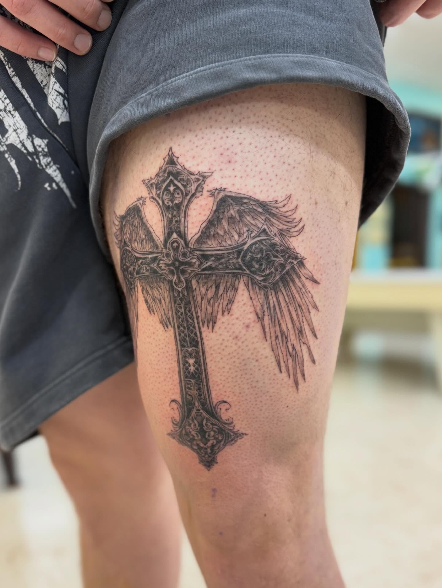 Cross with wings black and grey tattoo on the thigh by Levi Sawdon, Everett, Washington