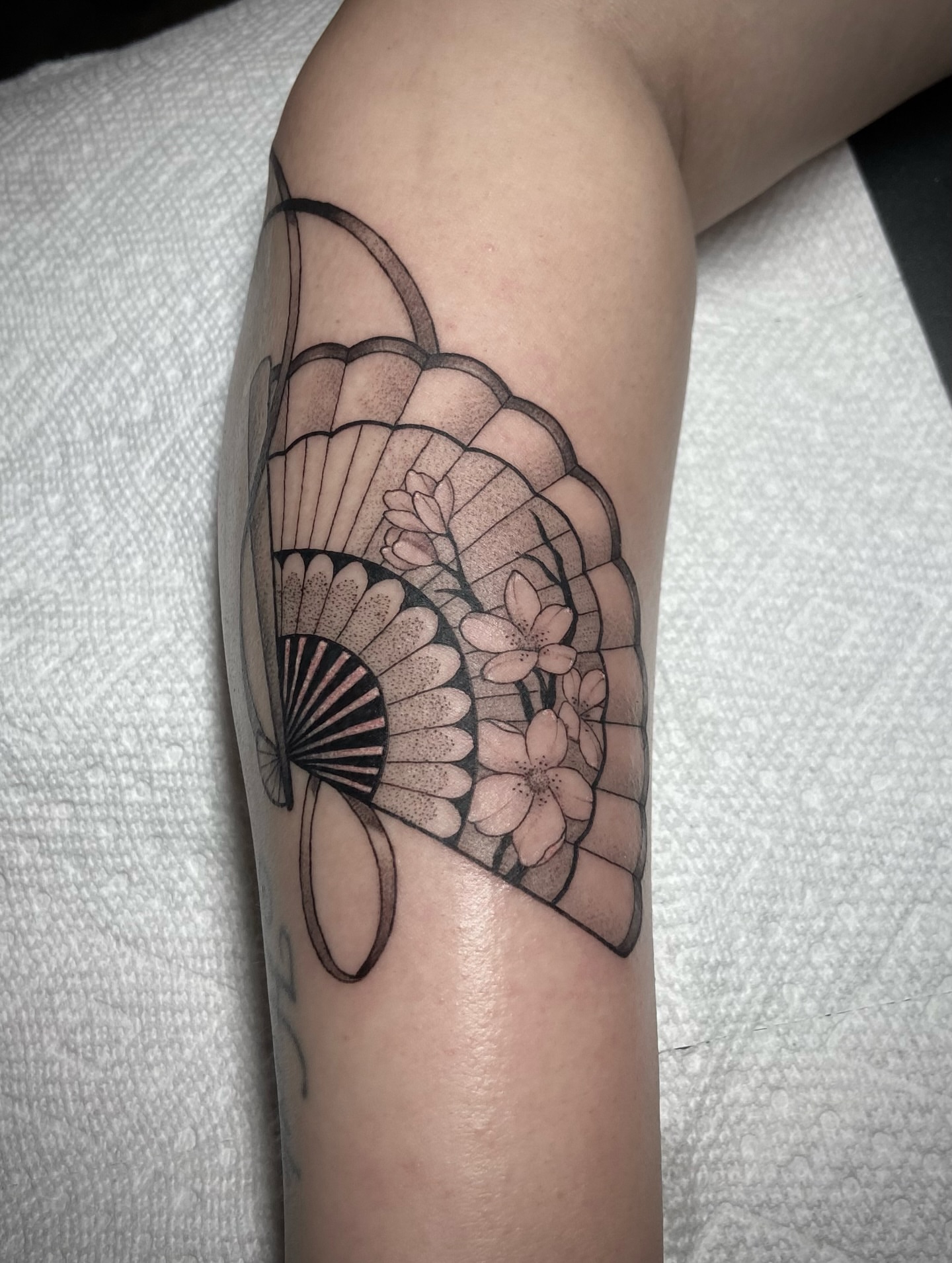 Fan and flowers black and grey tattoo on the forearm by Zac Byrd