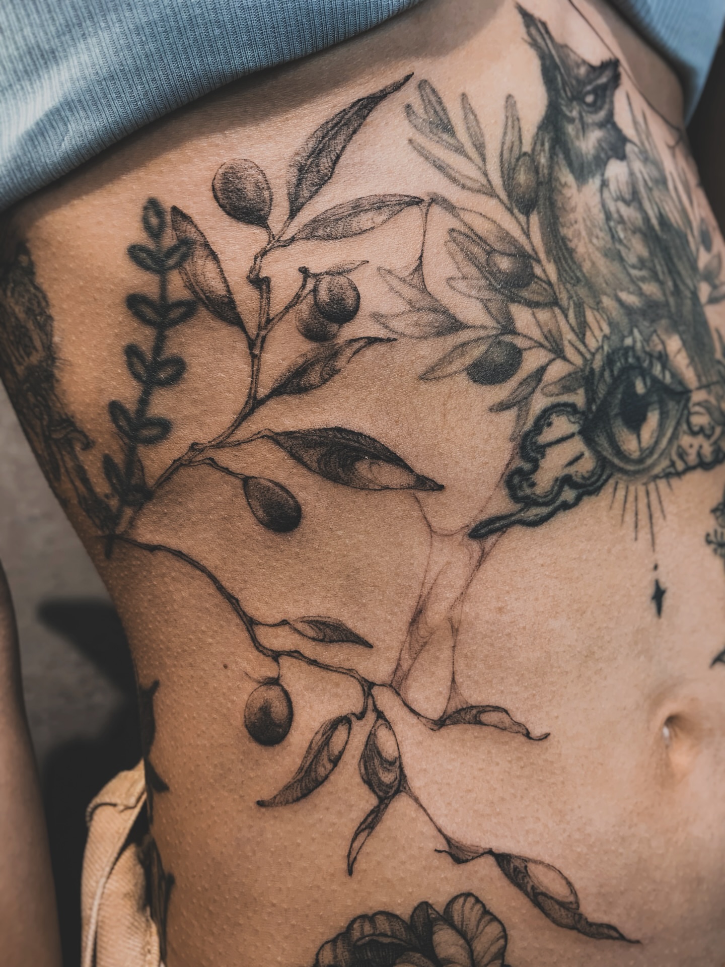 Olive branch and owl black and grey tattoo on the thigh by 21 tattooist