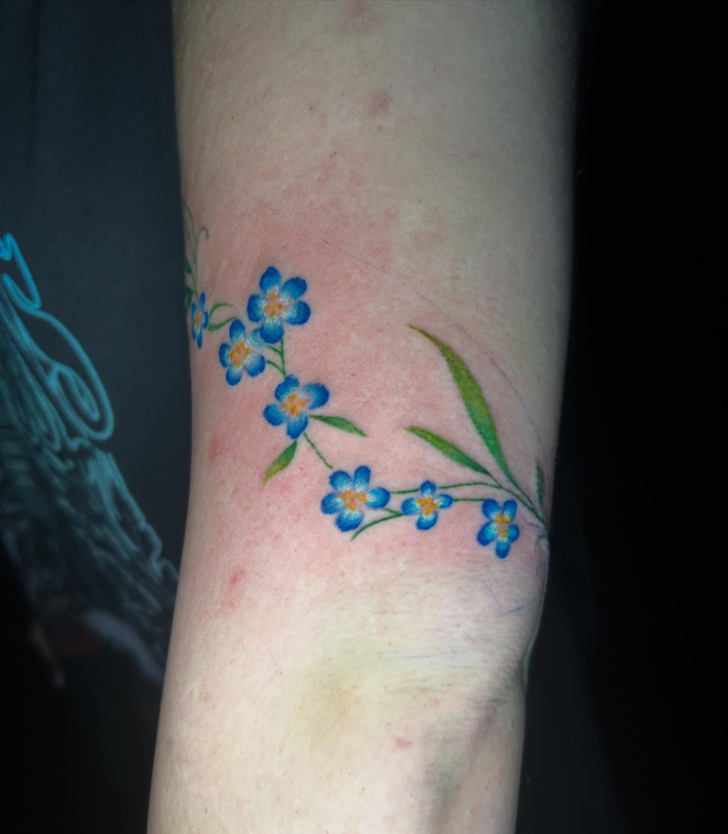 Blue forget-me-not flowers watercolor tattoo on the forearm by Mayhem Andrews