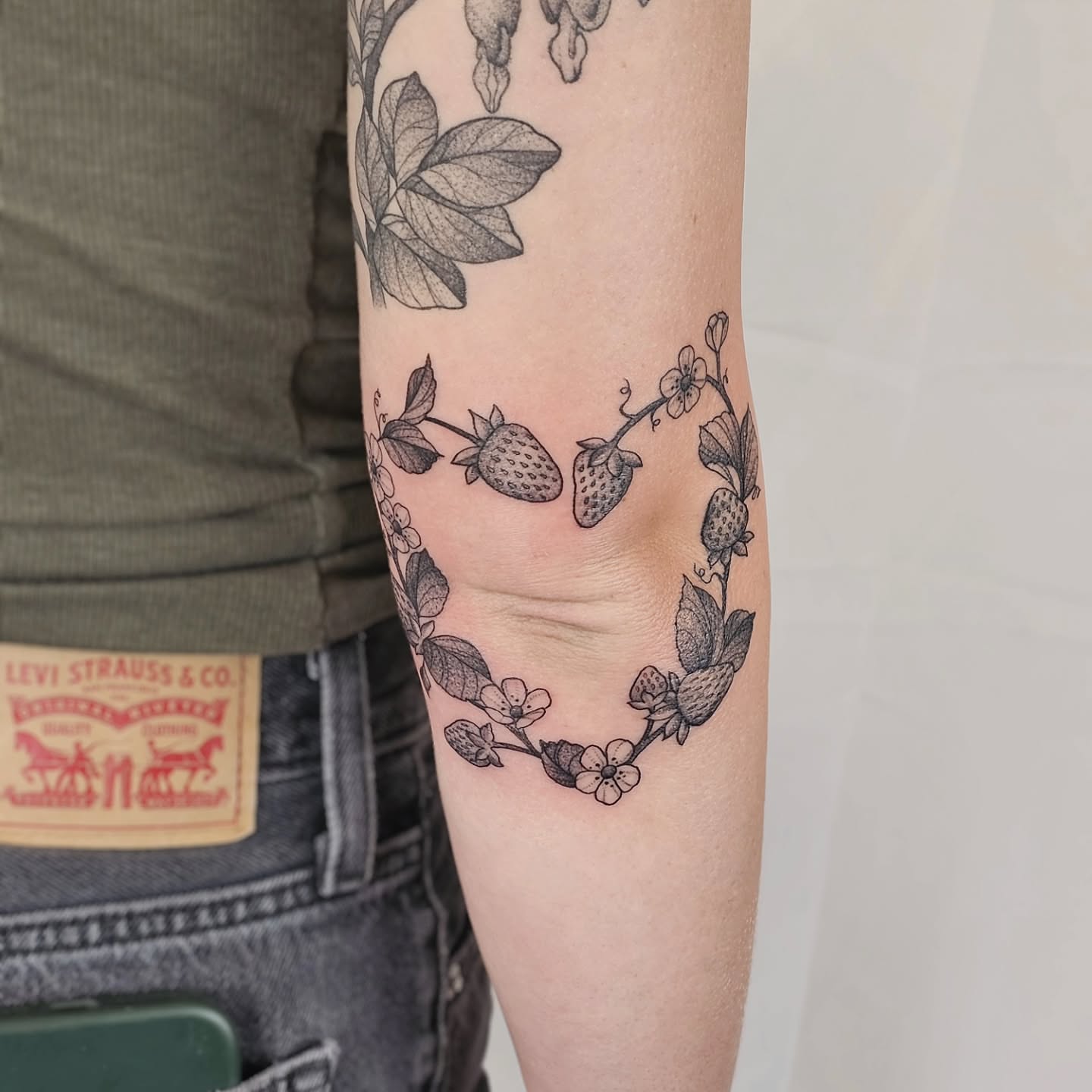 Strawberry wreath black and grey tattoo on the forearm by Kylie Lund