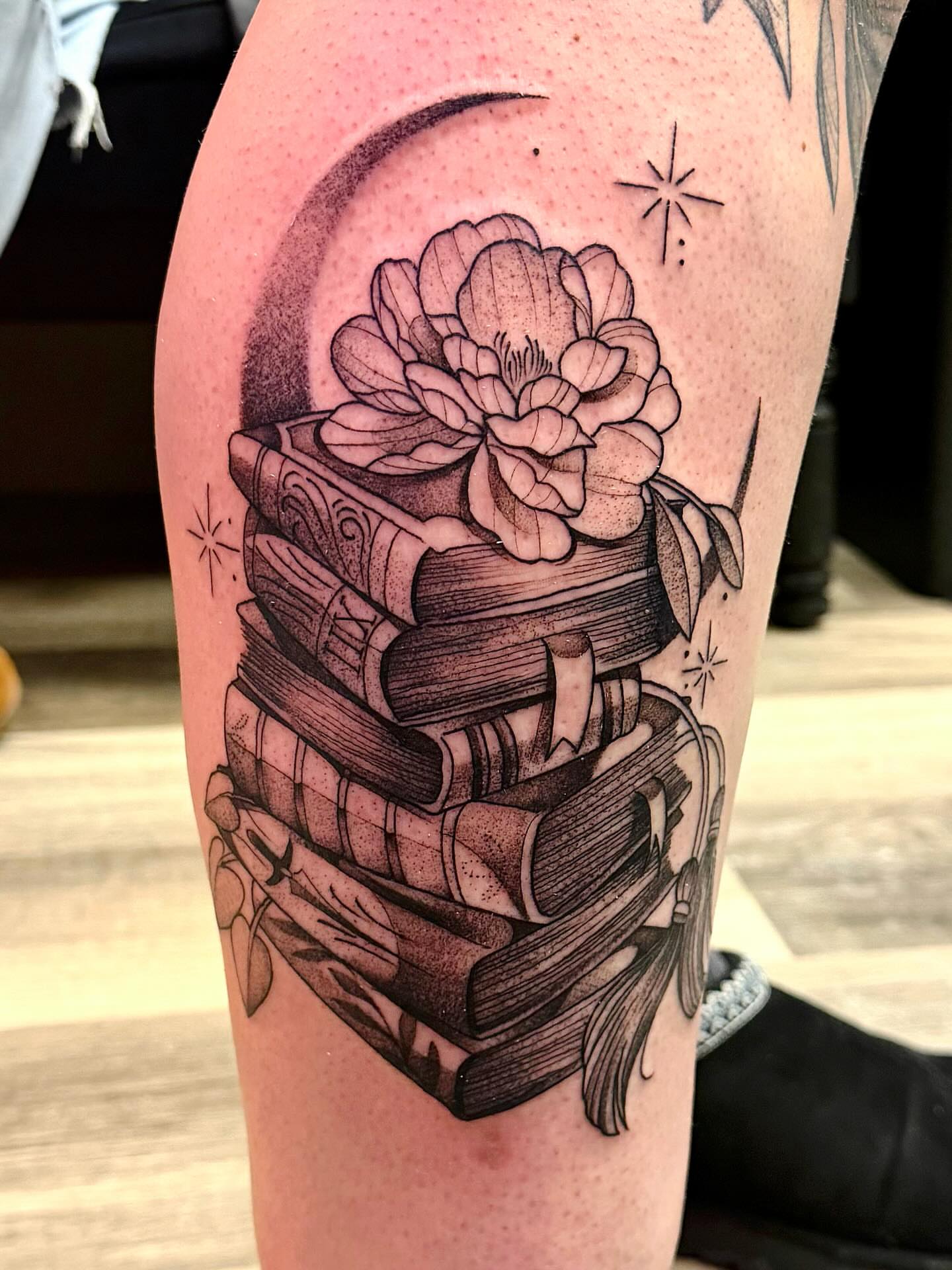 Stack of books with flower realism tattoo on the thigh by Emily
