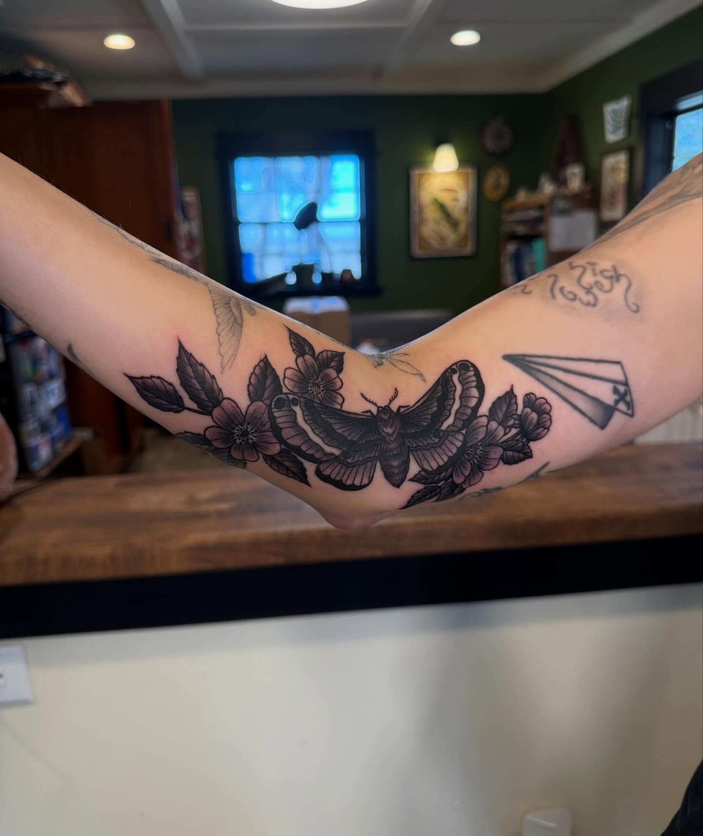 Moth and flowers black and grey tattoo on the forearm by Rebecca Basma Smith