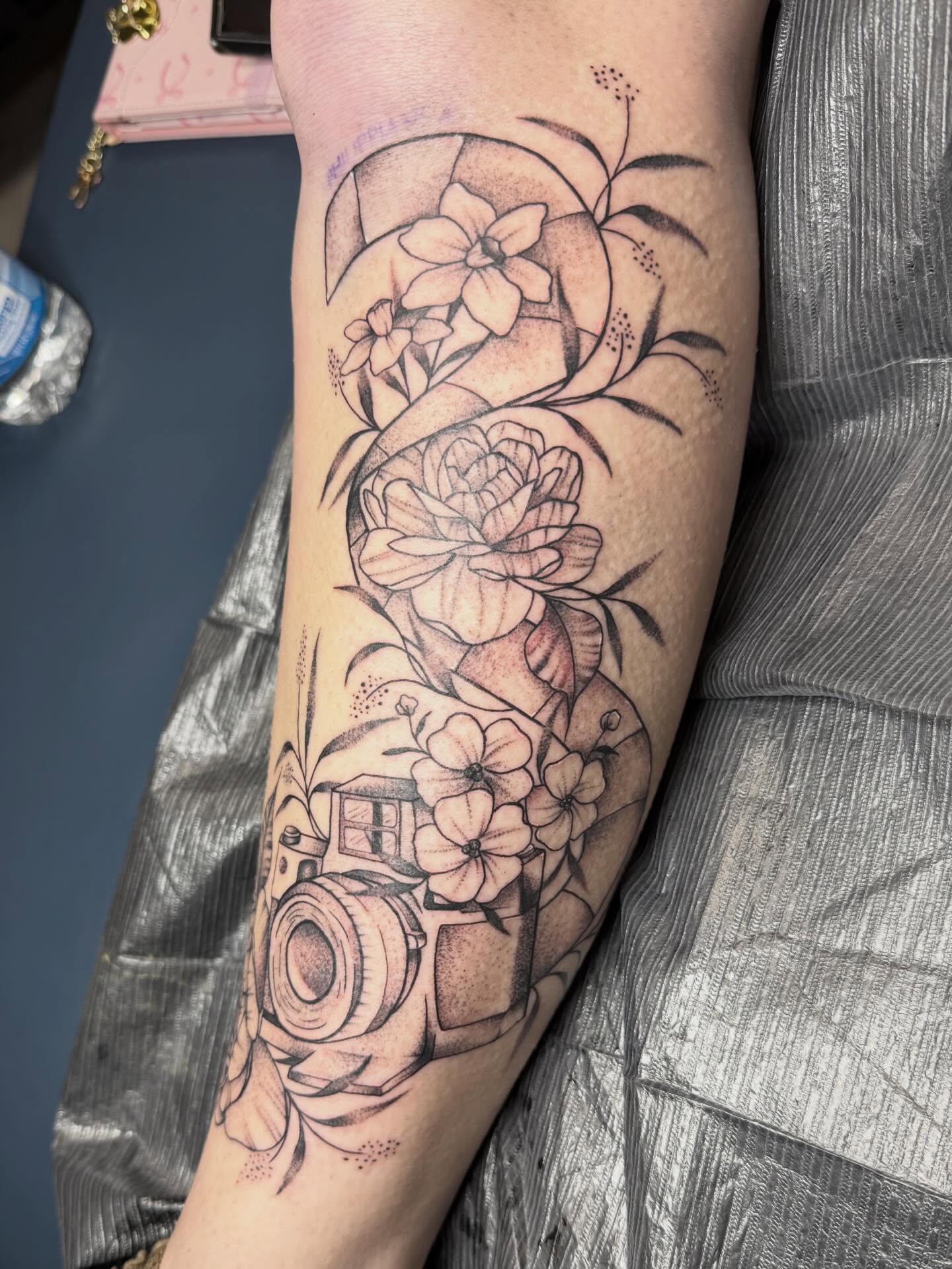 Camera and floral arrangement realism tattoo on the forearm by Abby