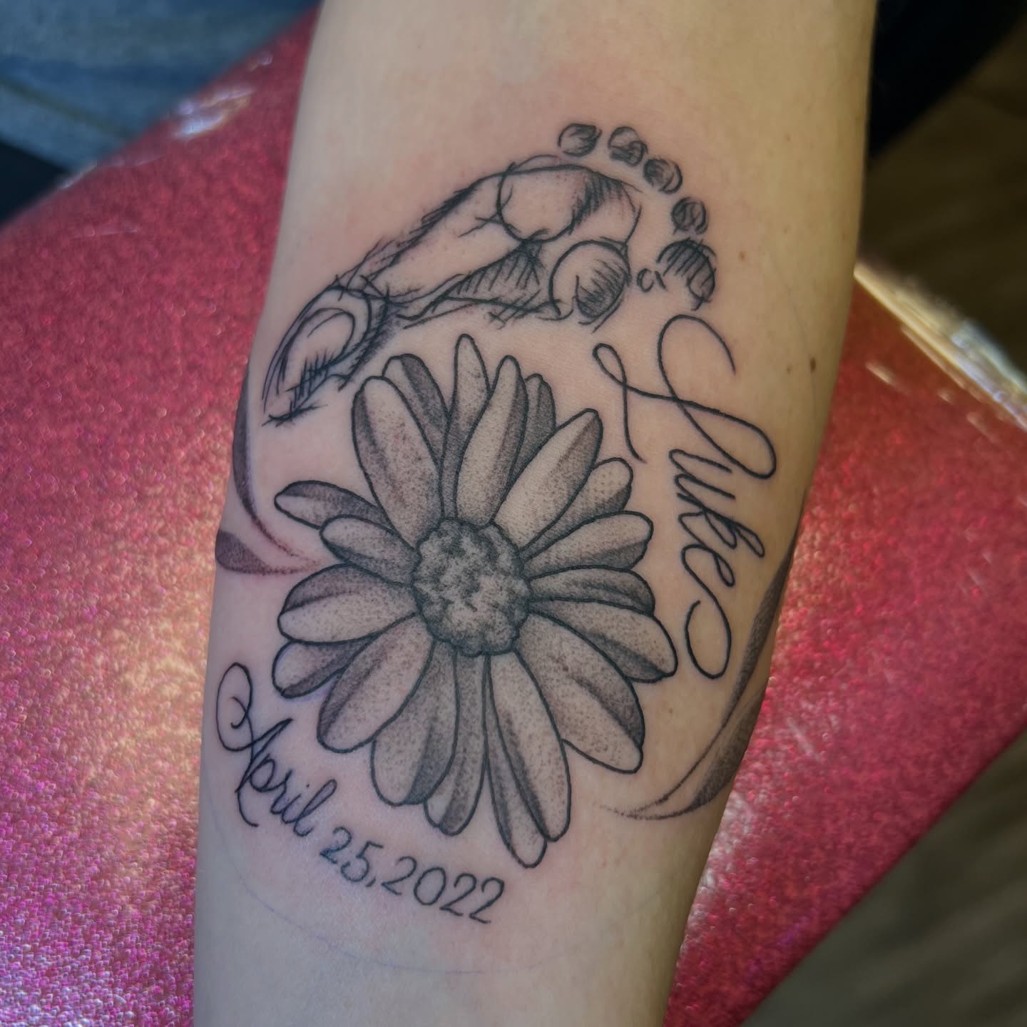 Daisy and footprints black and grey tattoo on the forearm by Dani McBay
