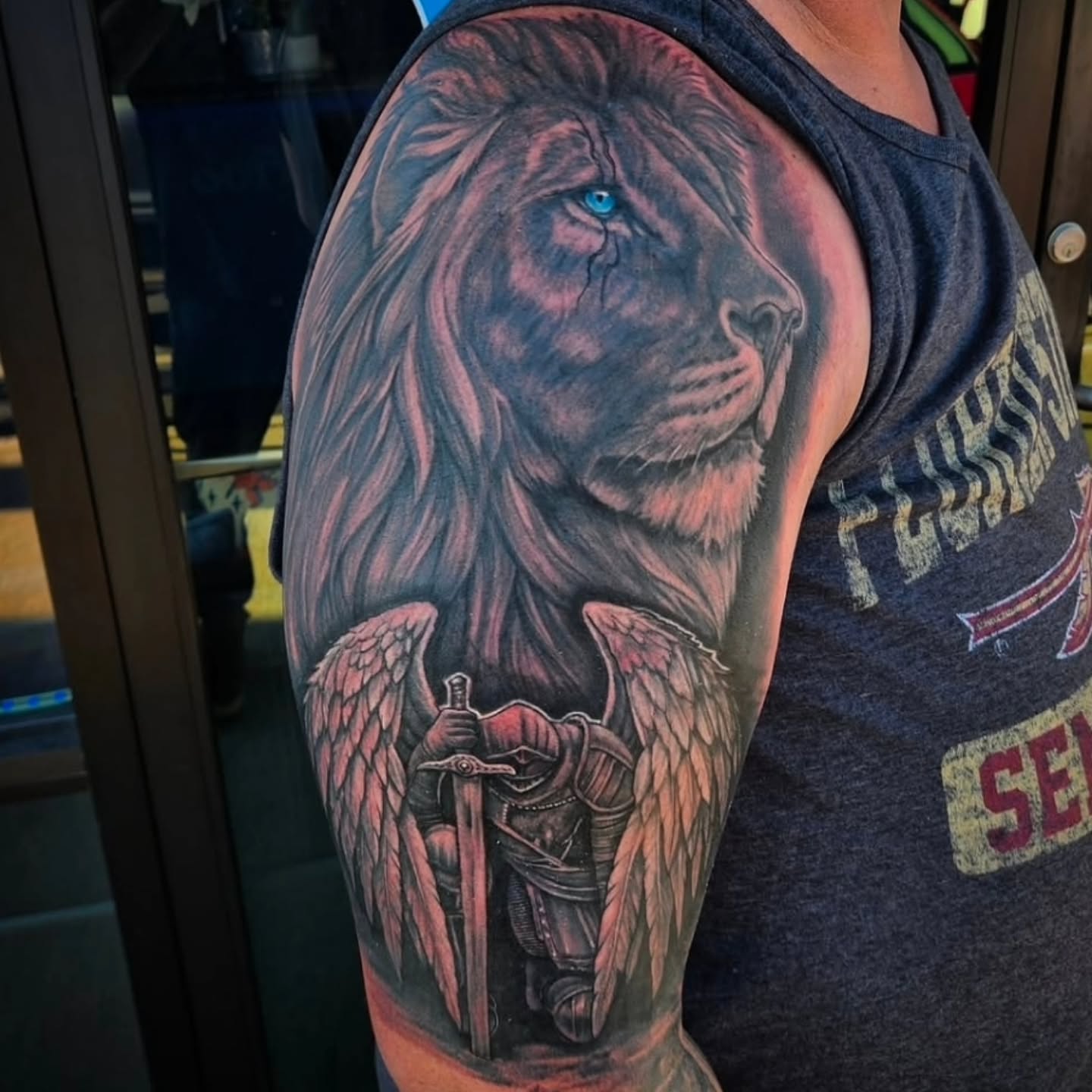 Lion with wings and sword realism tattoo on the upper arm by Mike Bugenhagen
