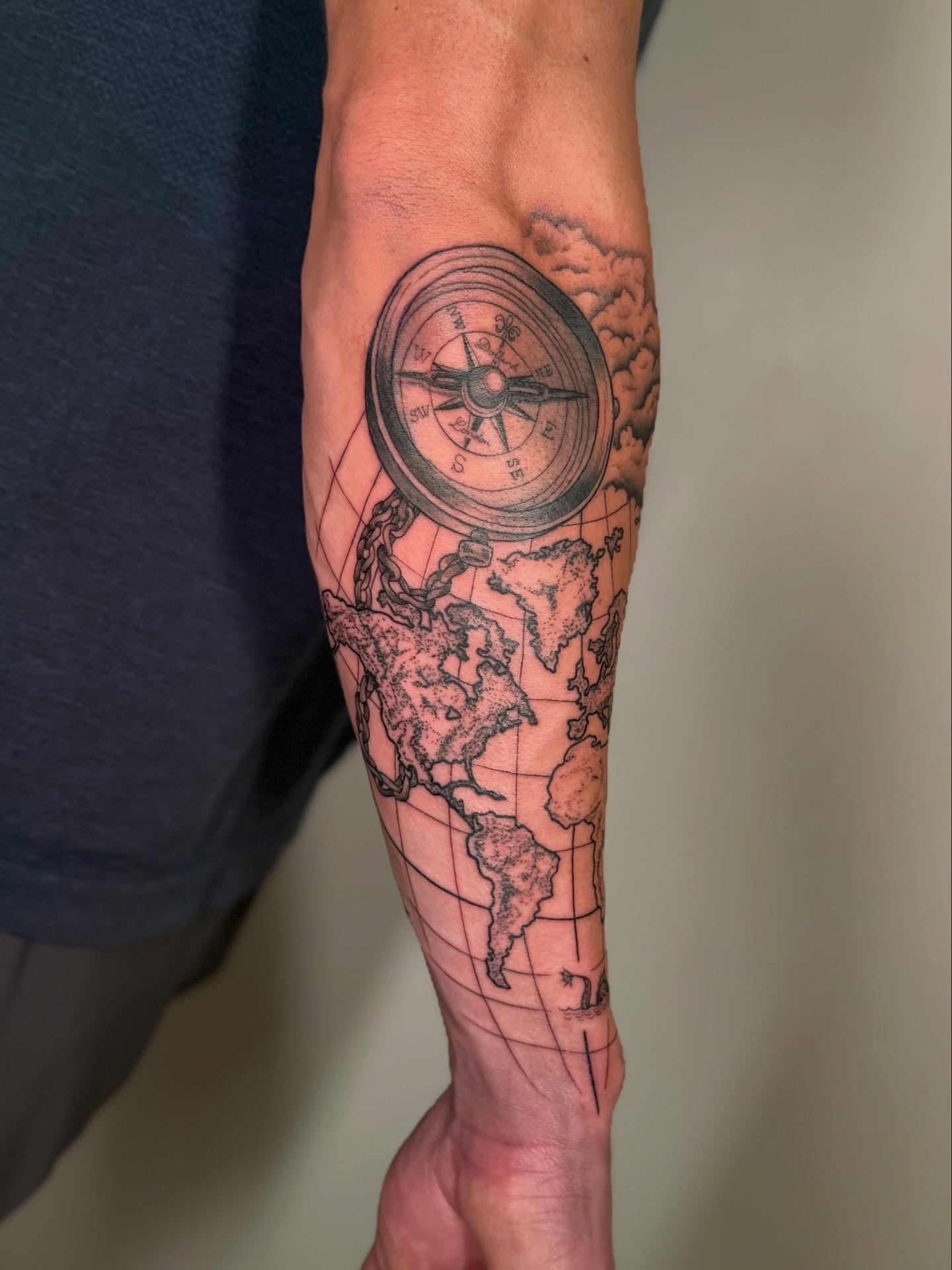 Compass and world map black and grey tattoo on the forearm by Kail