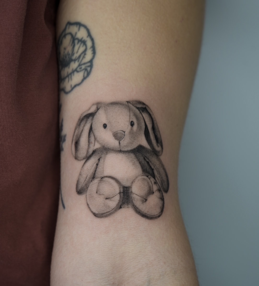 Stuffed bunny black and grey tattoo on the forearm by Blackwork & microrealism tattoos
