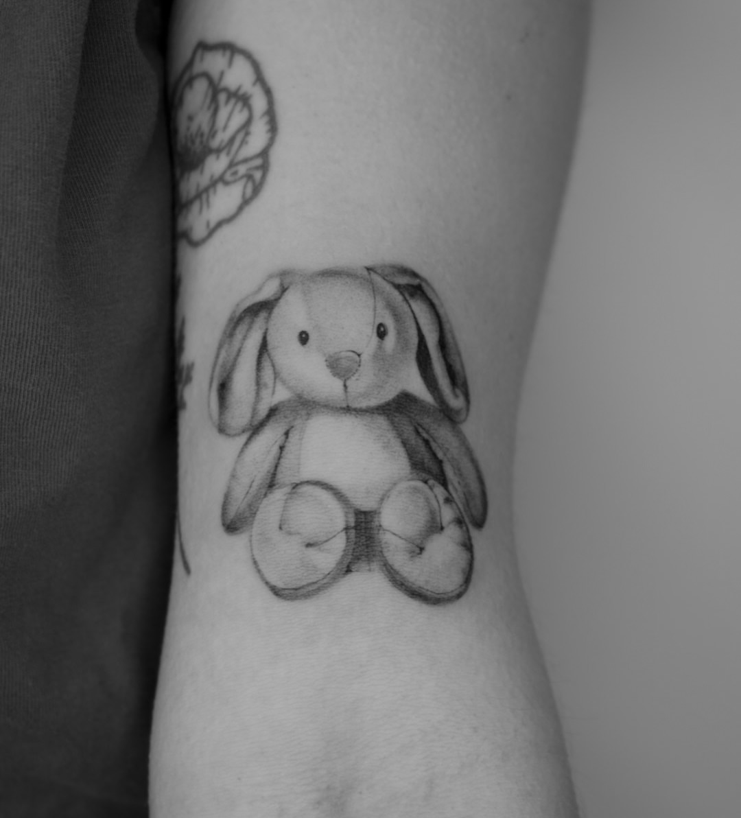 Stuffed bunny black and grey tattoo on the forearm by Blackwork & microrealism tattoos