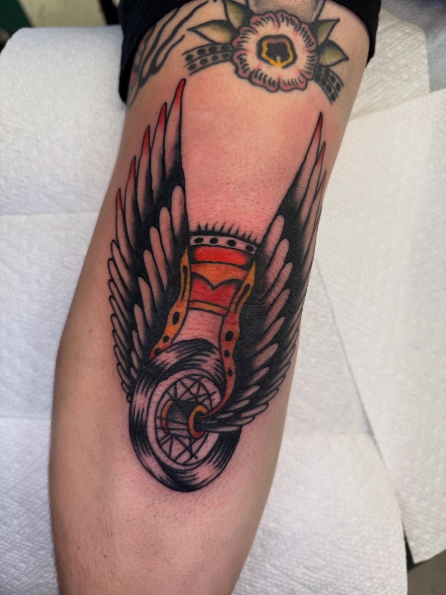 Motorcycle wheel with wings American traditional tattoo on the forearm by Cody Petkus
