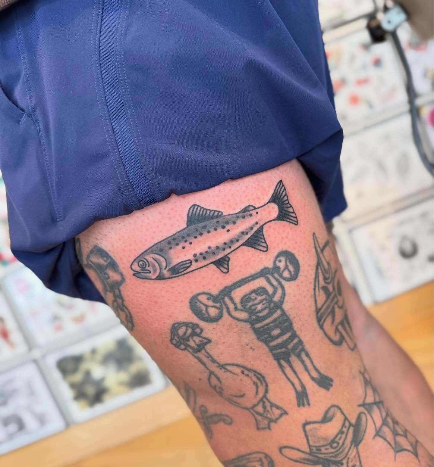 Fish and weightlifter black and grey tattoo on the thigh by Elle Yax