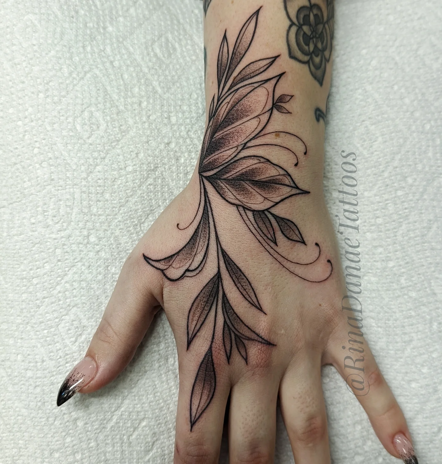 Feather black and grey tattoo on the hand by Rina Danaé Tattoo🌿