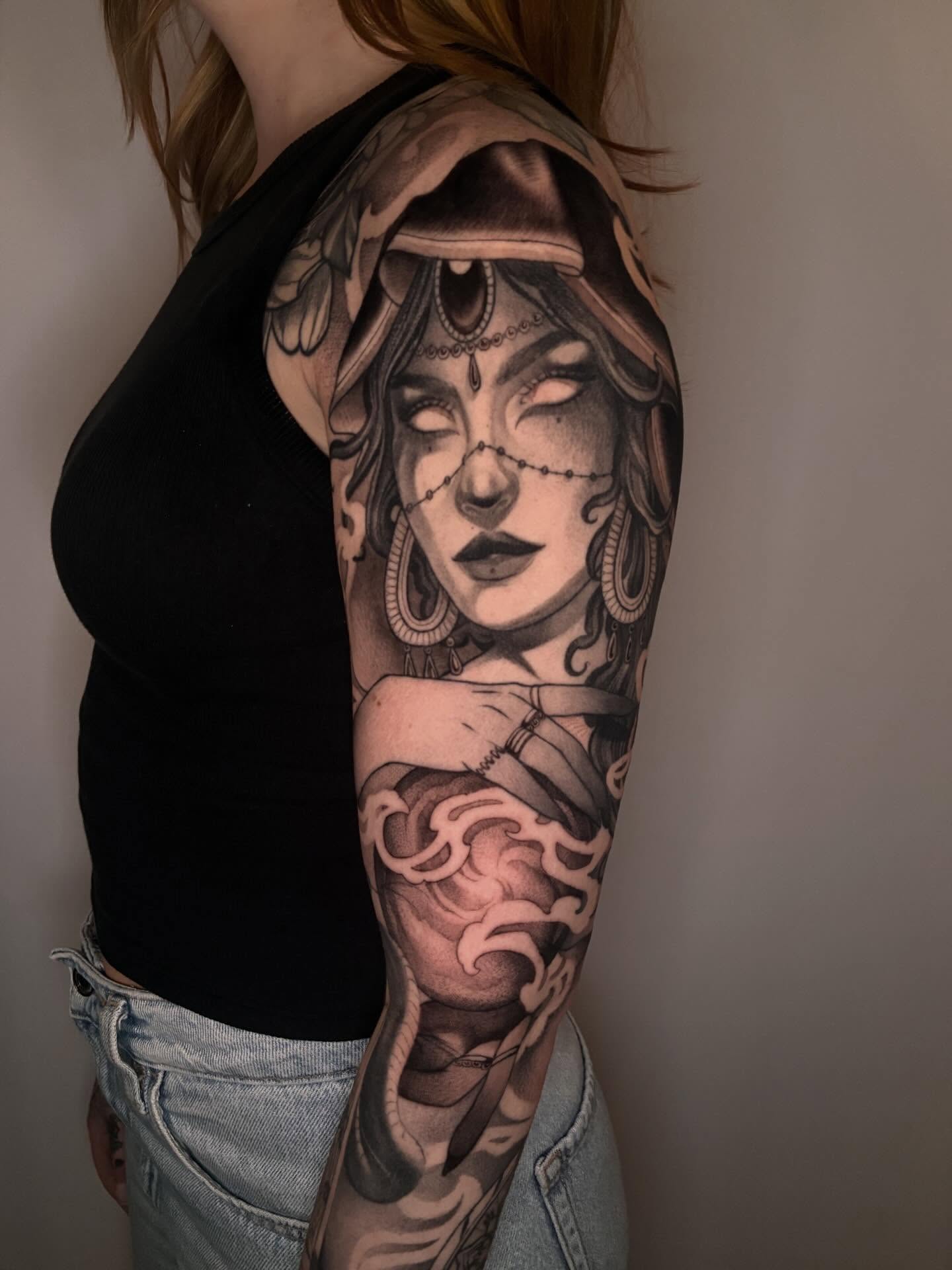 Woman with headdress realism tattoo on the upper arm by Carol Jacky