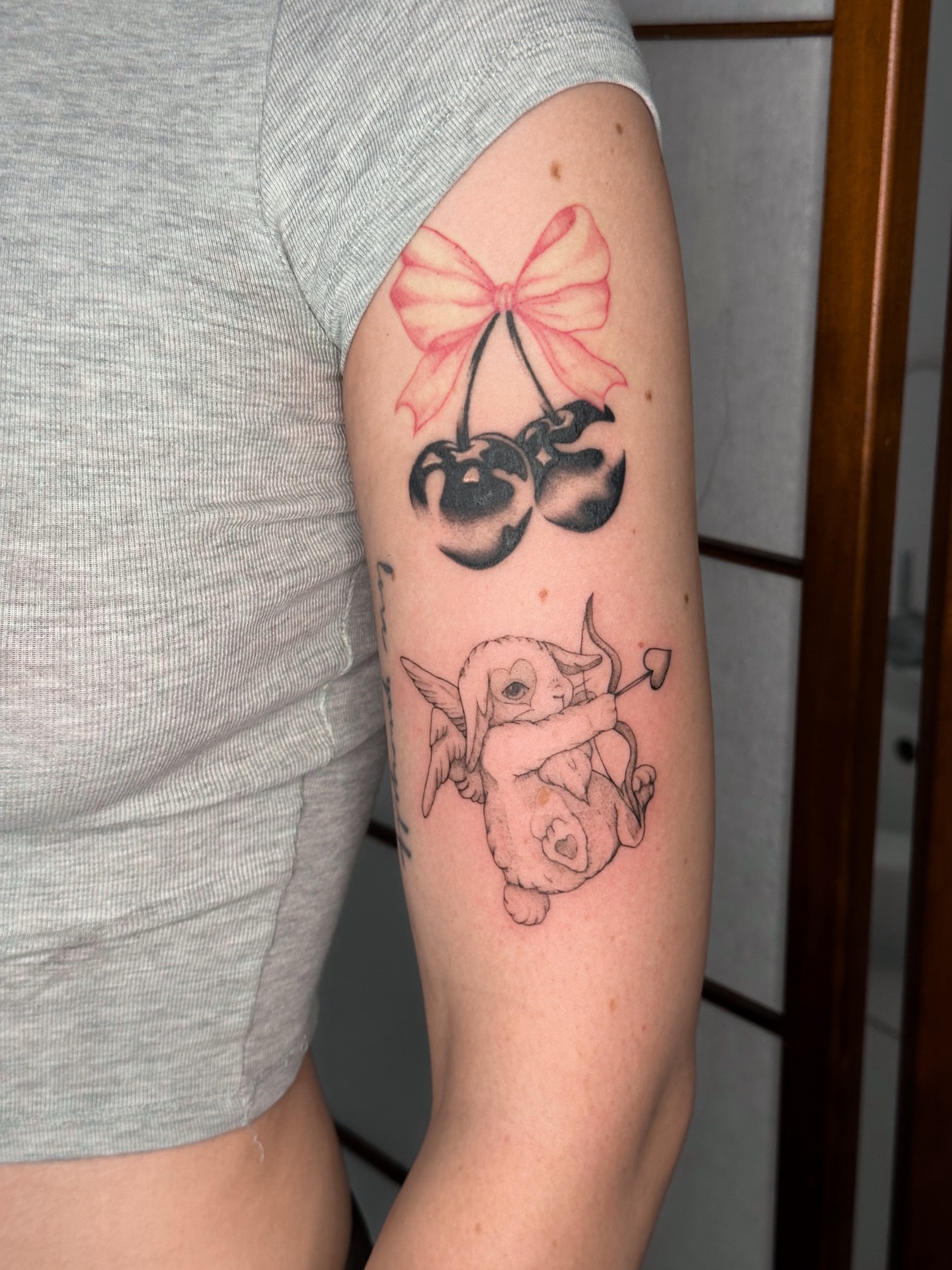 Cherries with bow black and grey tattoo on the forearm by Mila, Riga, Latvia