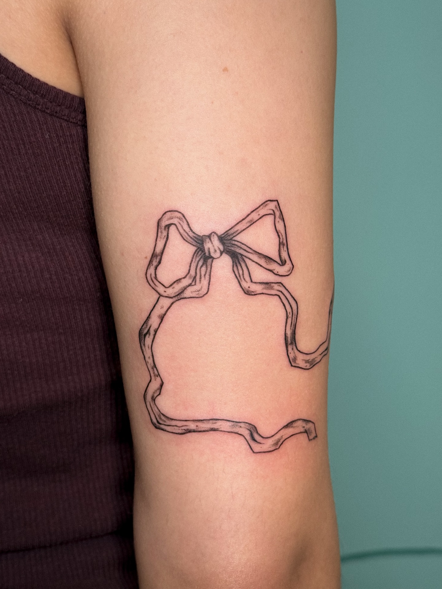 Bow fine line tattoo on the forearm by madison