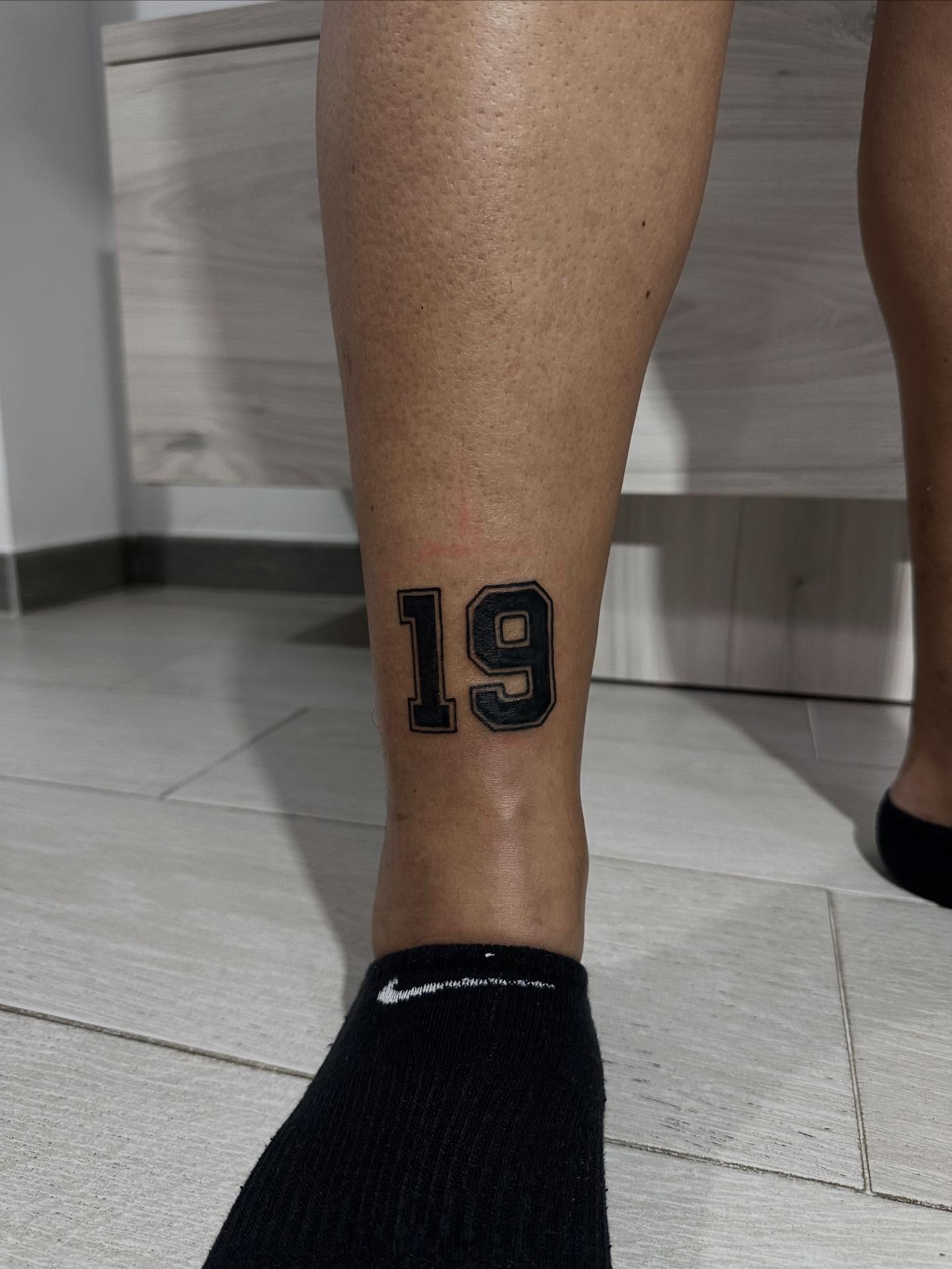 Number 19 black and grey tattoo on the calf by Kunaytattoo