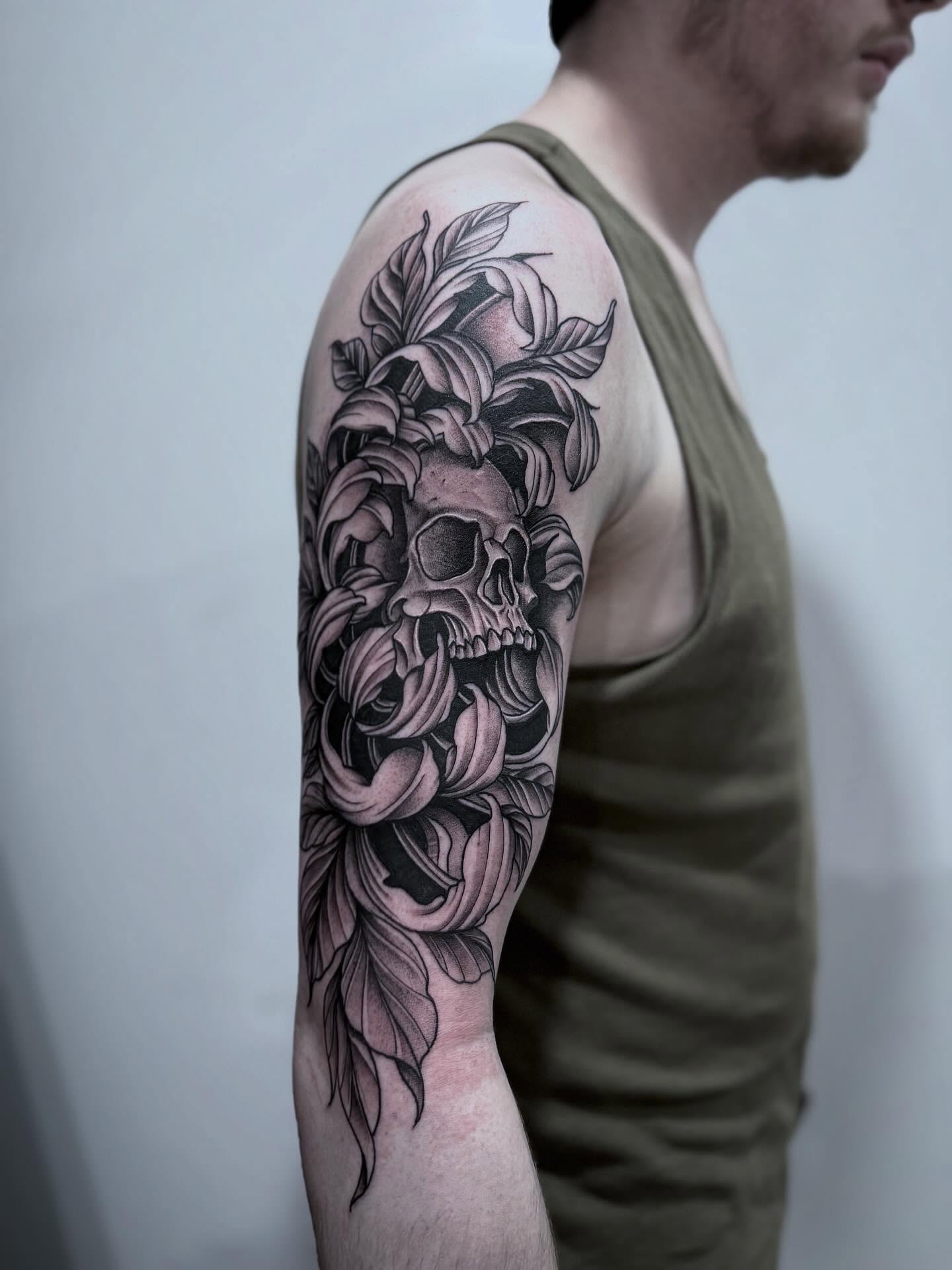 Skull and leaves realism tattoo on the upper arm by Tattoo Ottawa