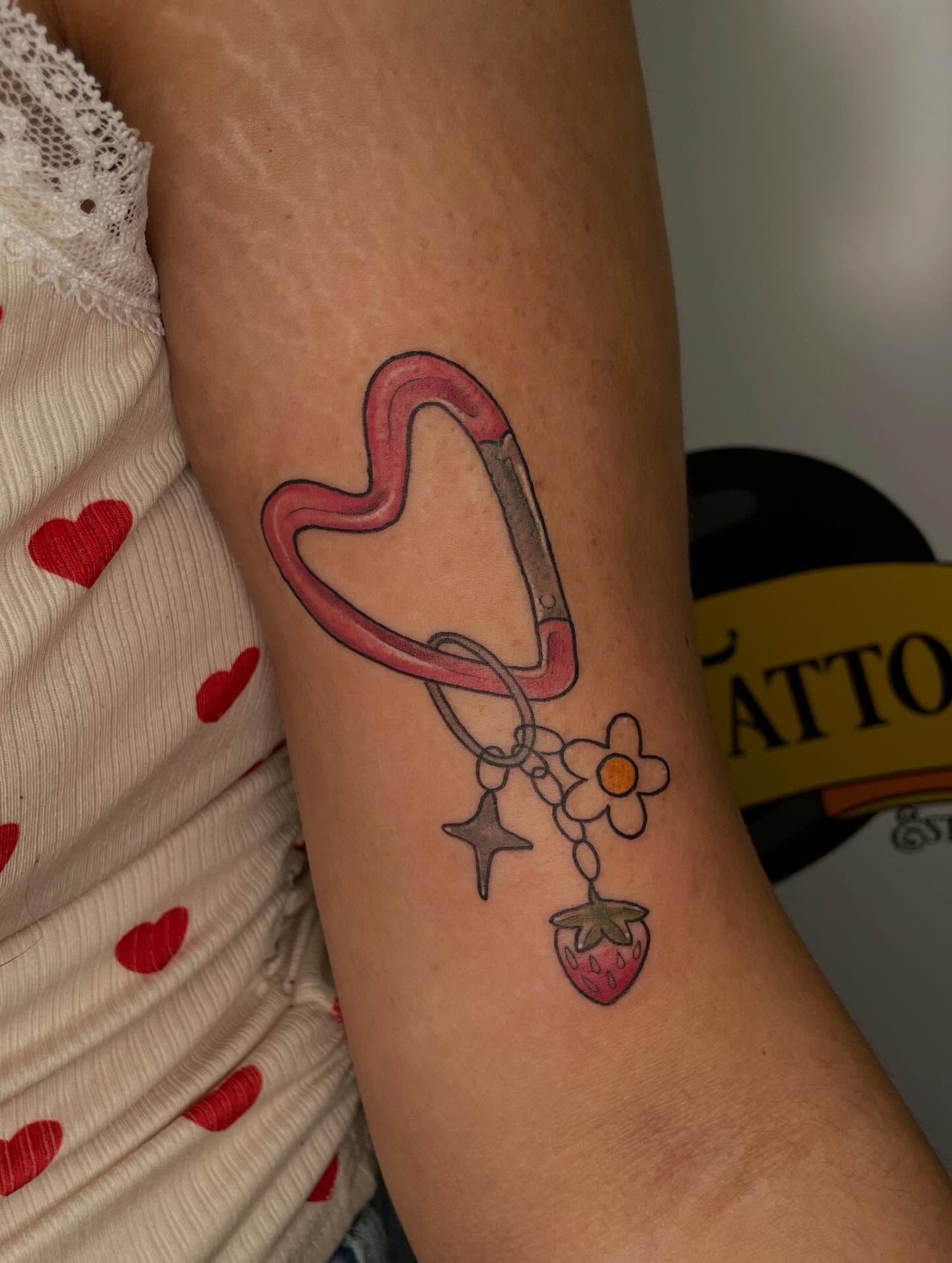 Heart-shaped carabiner with charms new school tattoo on the forearm by Stevie Timmreck, Utica, Michigan