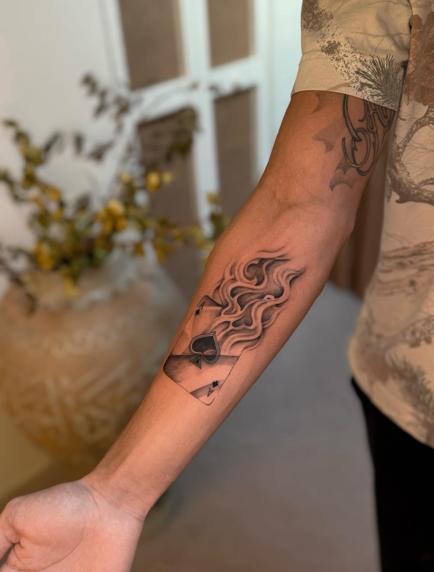 Playing card with flames black and grey tattoo on the forearm by Christian Guerrero