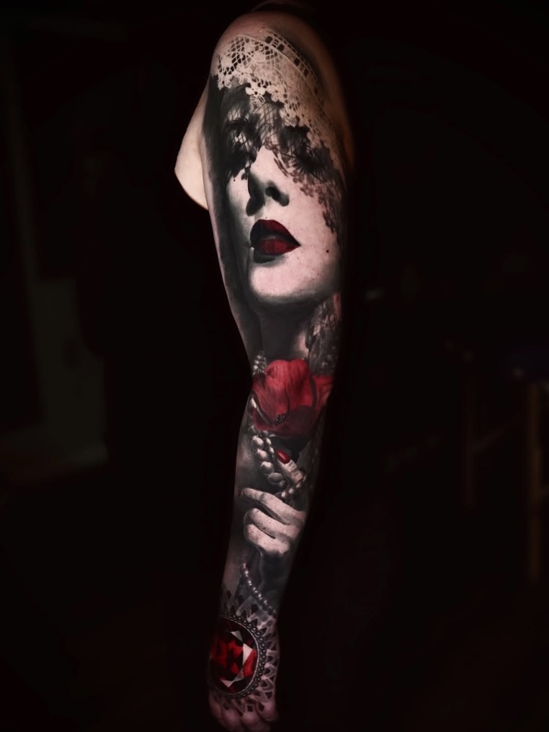 Woman with red flower and jewel realism tattoo on the forearm by Chris Bowling