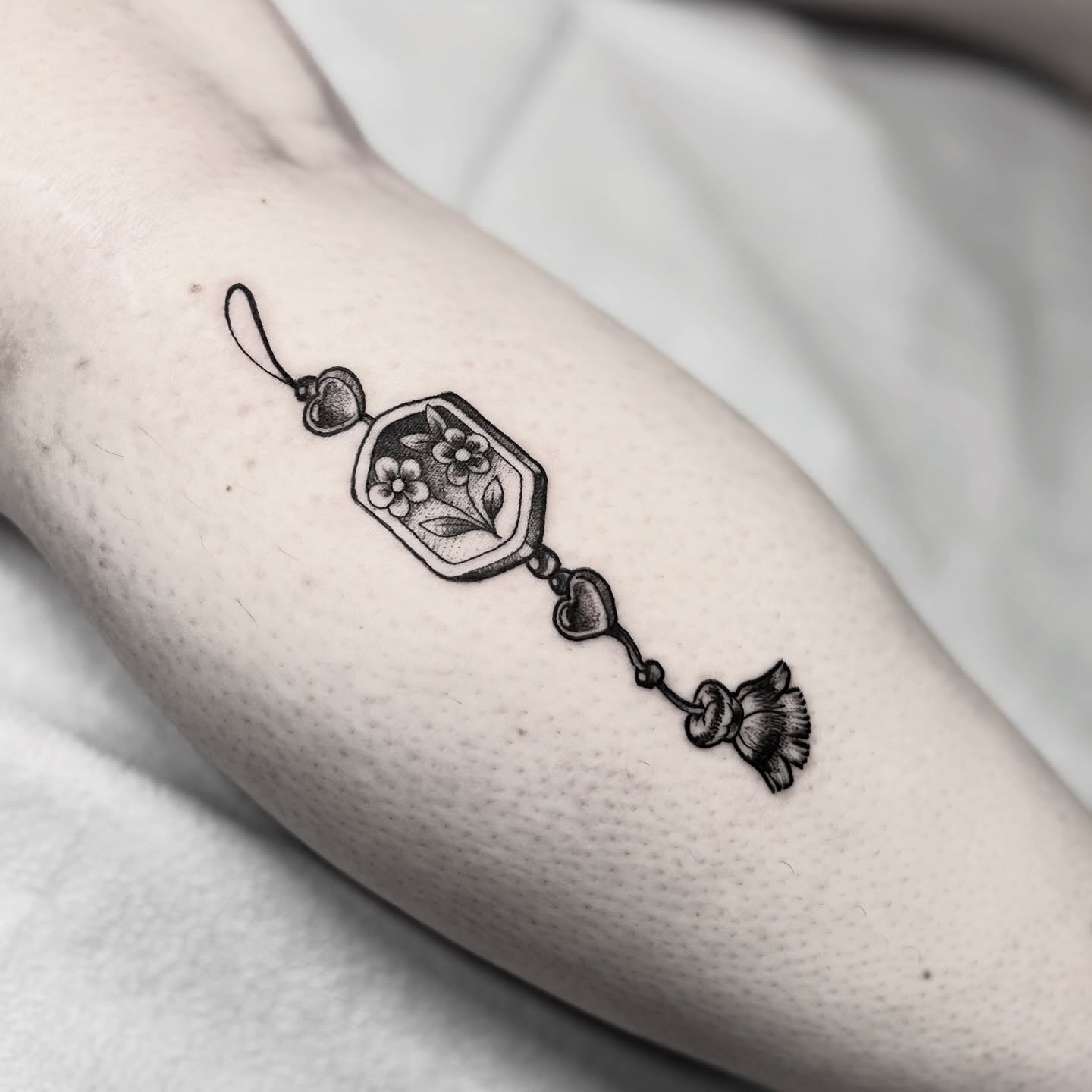 Pendant with flowers black and grey tattoo on the forearm by Alex Santaloci