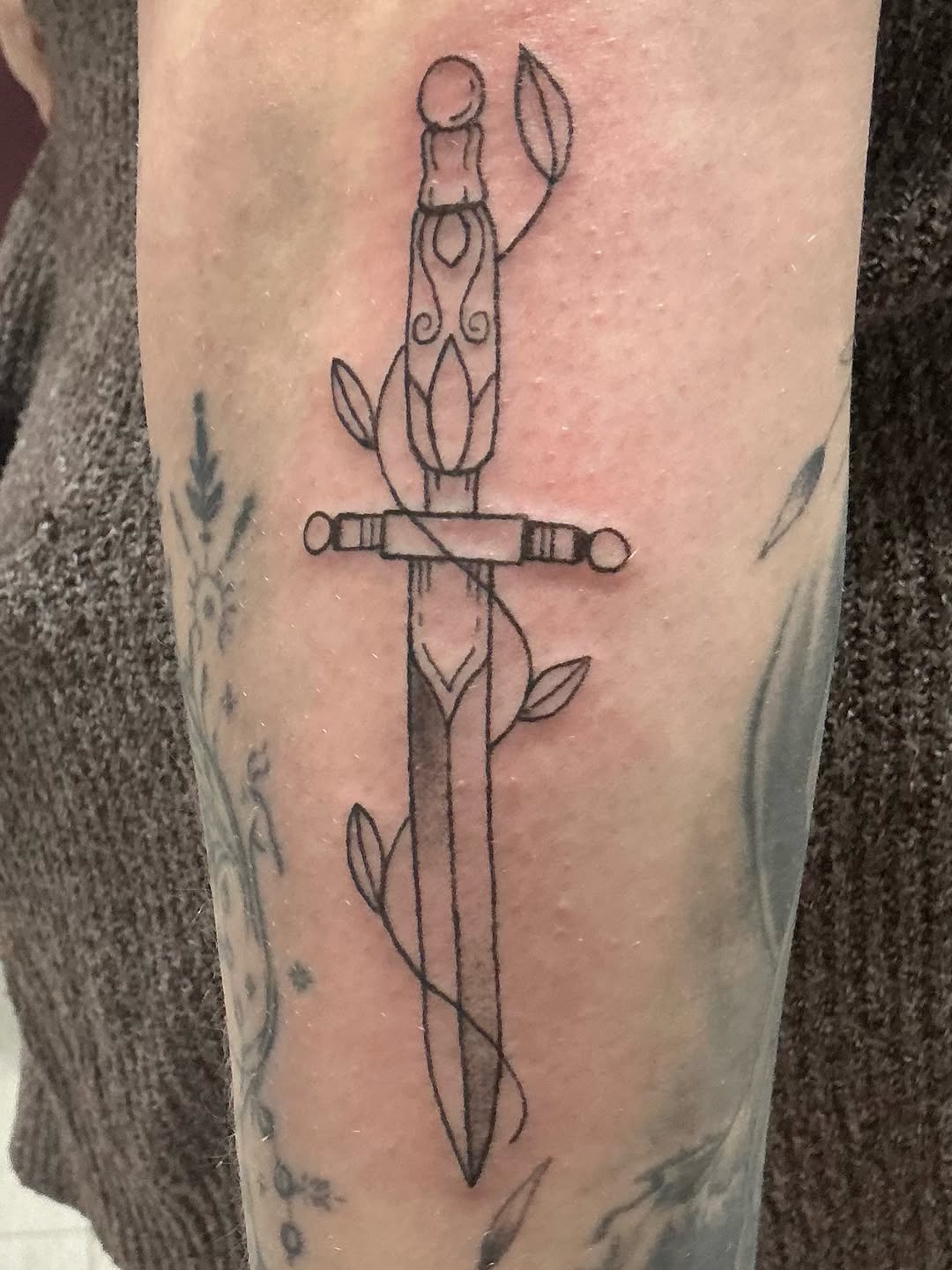 Sword with vines minimalist tattoo on the forearm by Isaac Mccavitt