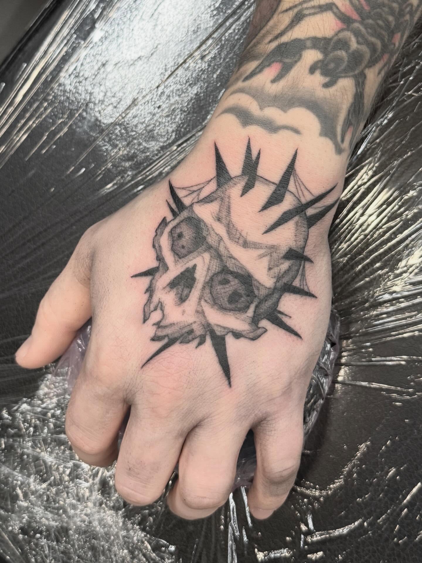 Skull and spikes black and grey tattoo on the hand by Peter Harren